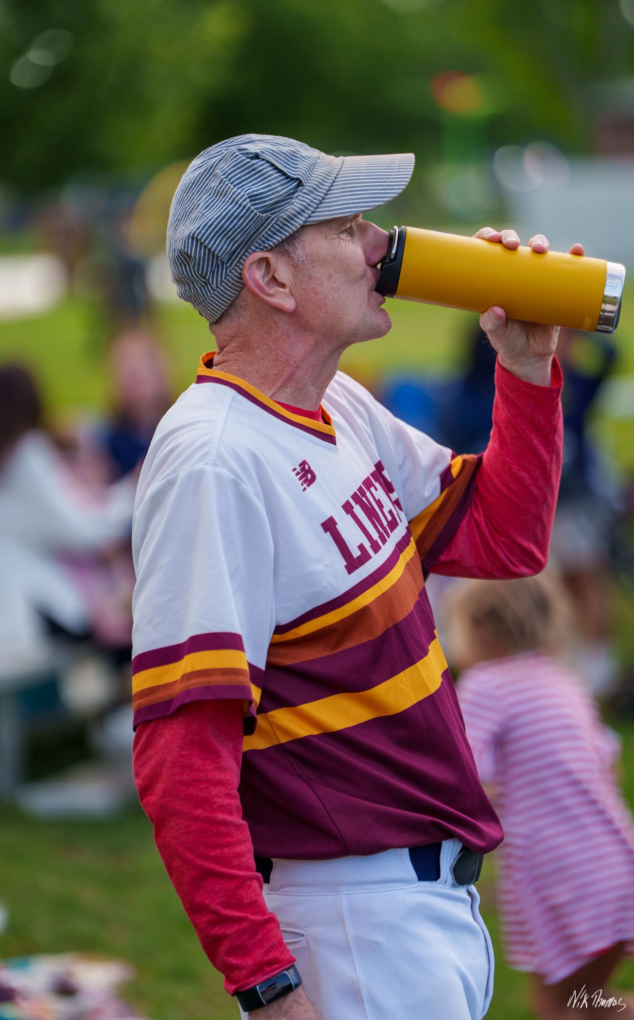 Baseball player in Lions uniform drinking from yellow water bottle during outdoor game.