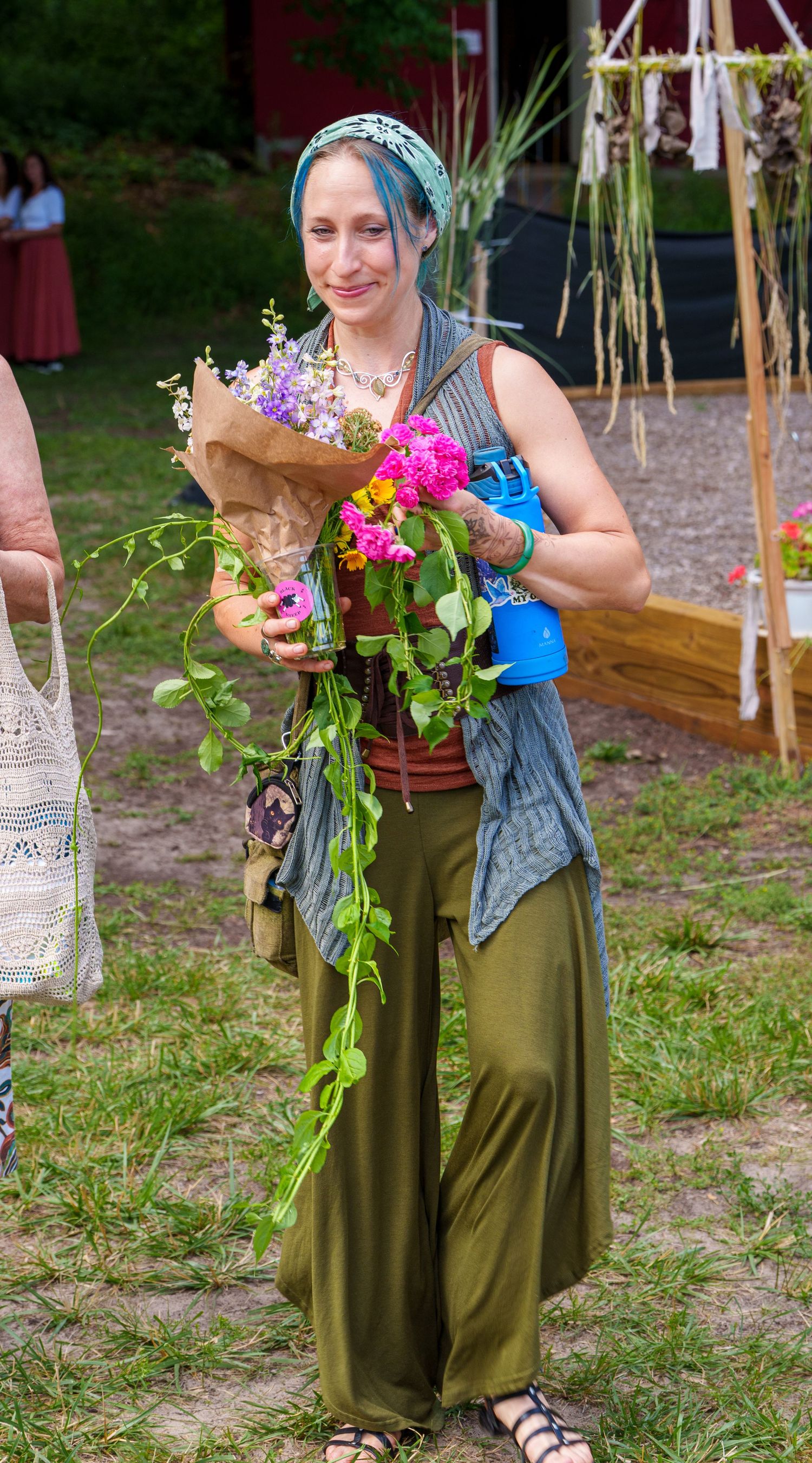 Woman with blue hair holding vibrant bouquet of wildflowers at outdoor festival event.
