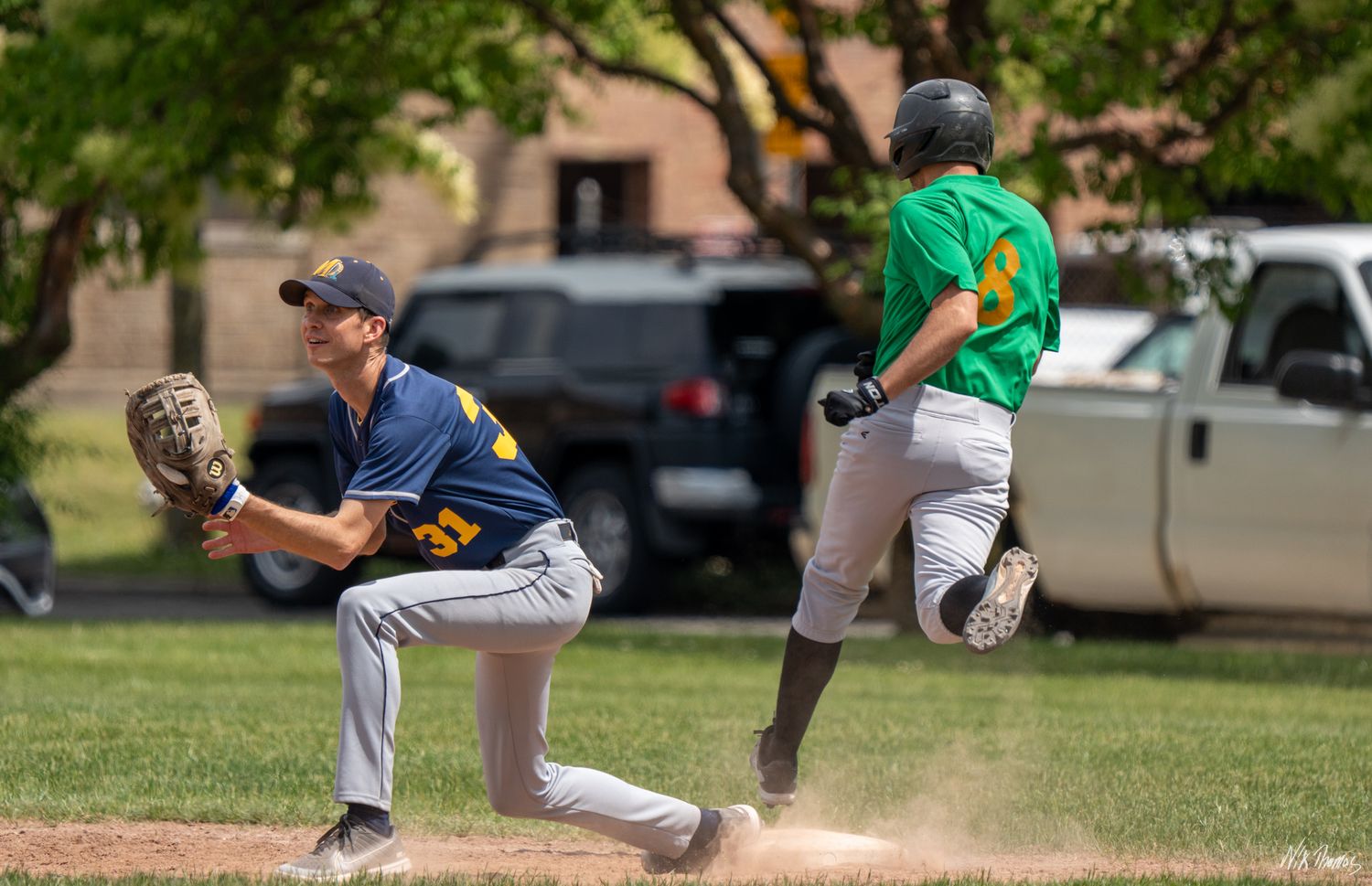 Baseball player running to first base as fielder stretches to catch the ball during an outdoor game.