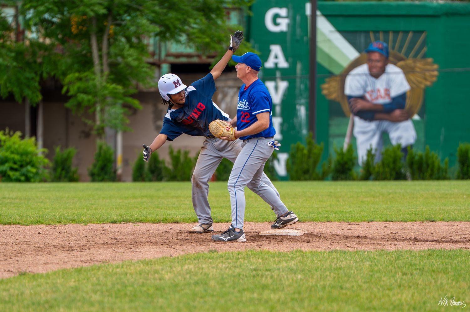 Two baseball players collide at a base during a game on a green grass field with a mural visible in the background.