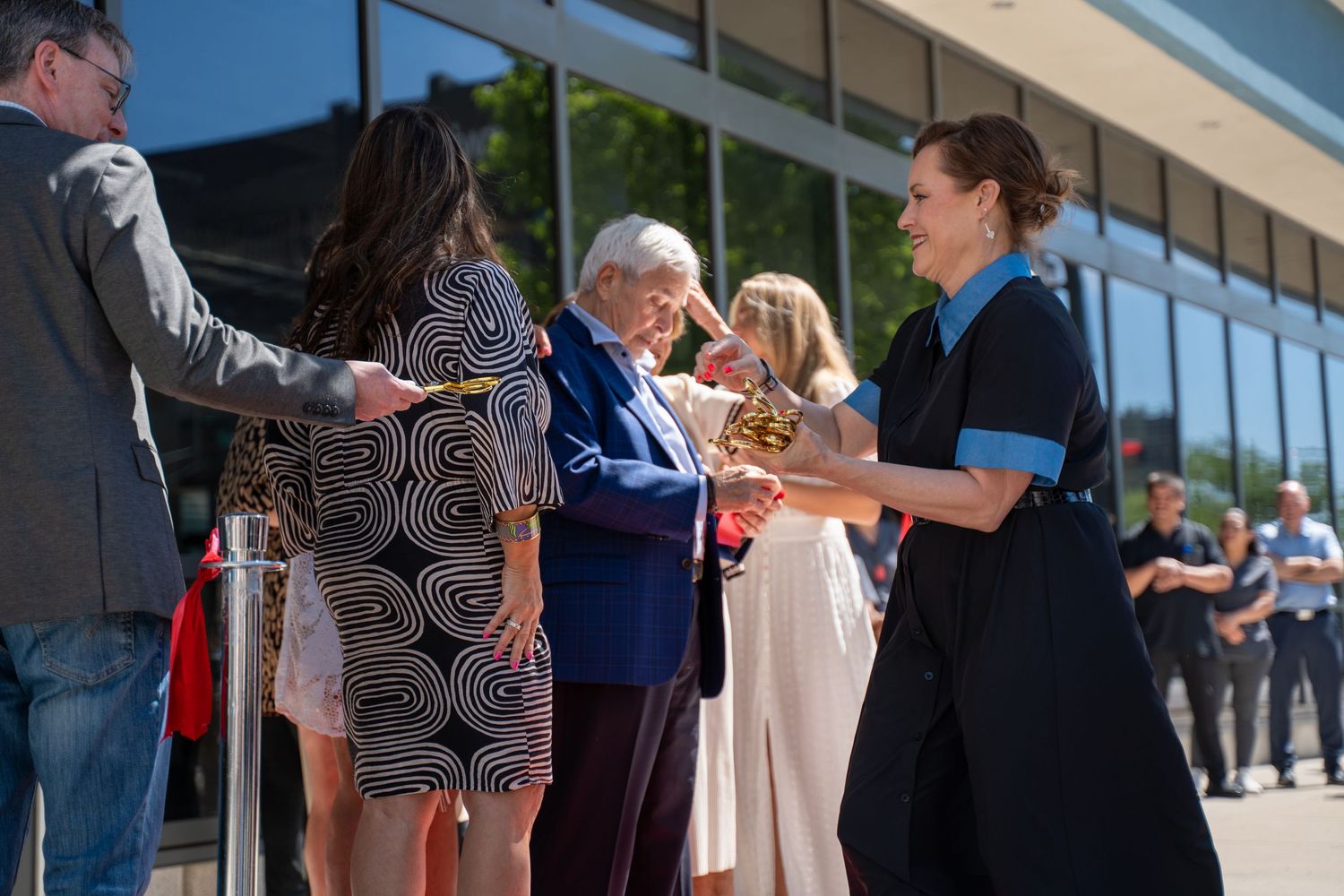 Group of people greeting elderly man outside modern building on sunny day.