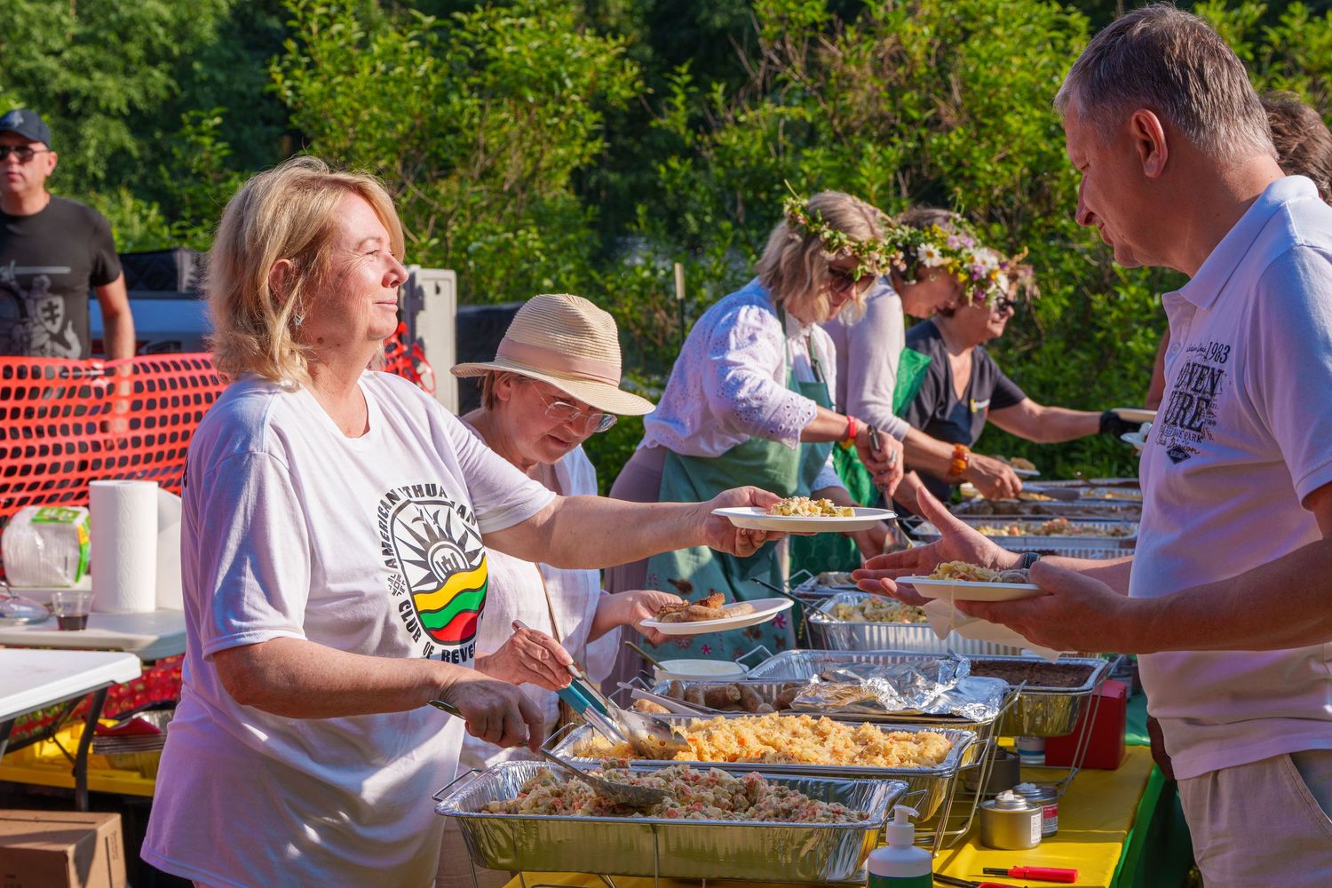 People serving food at an outdoor buffet line during a Lithuanian cultural festival event.