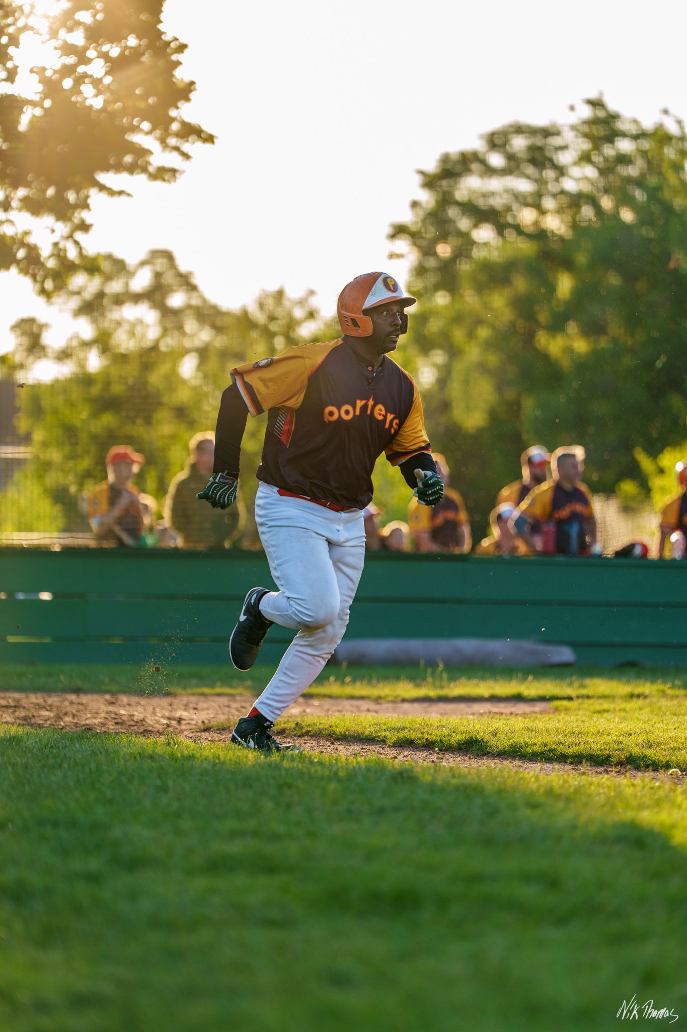 Baseball player in brown and black uniform running bases during golden hour sunset game.