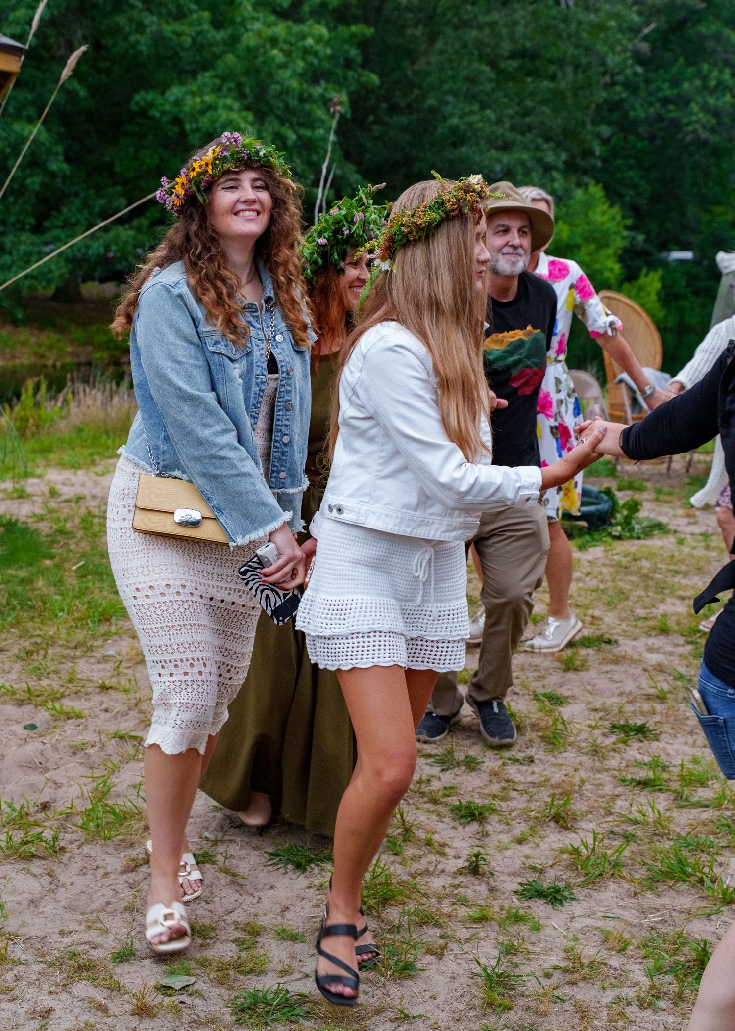 Young women wearing floral wreaths dancing joyfully at an outdoor Lithuanian midsummer festival.