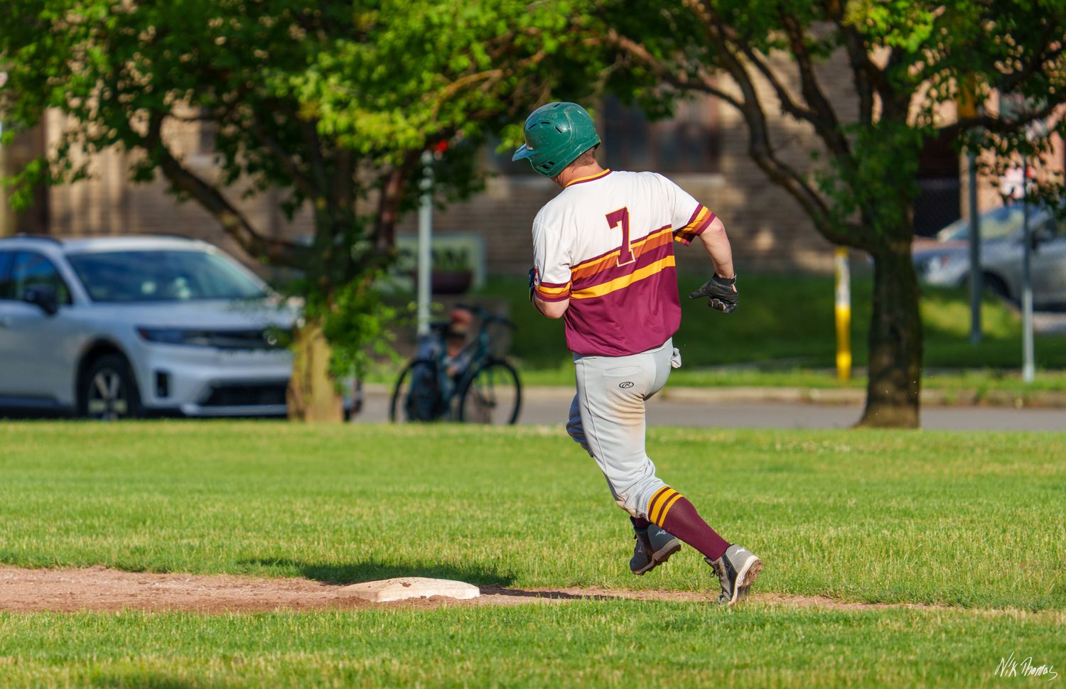 Baseball player wearing number 7 rounds a base during a sunny outdoor game on a green grass field.