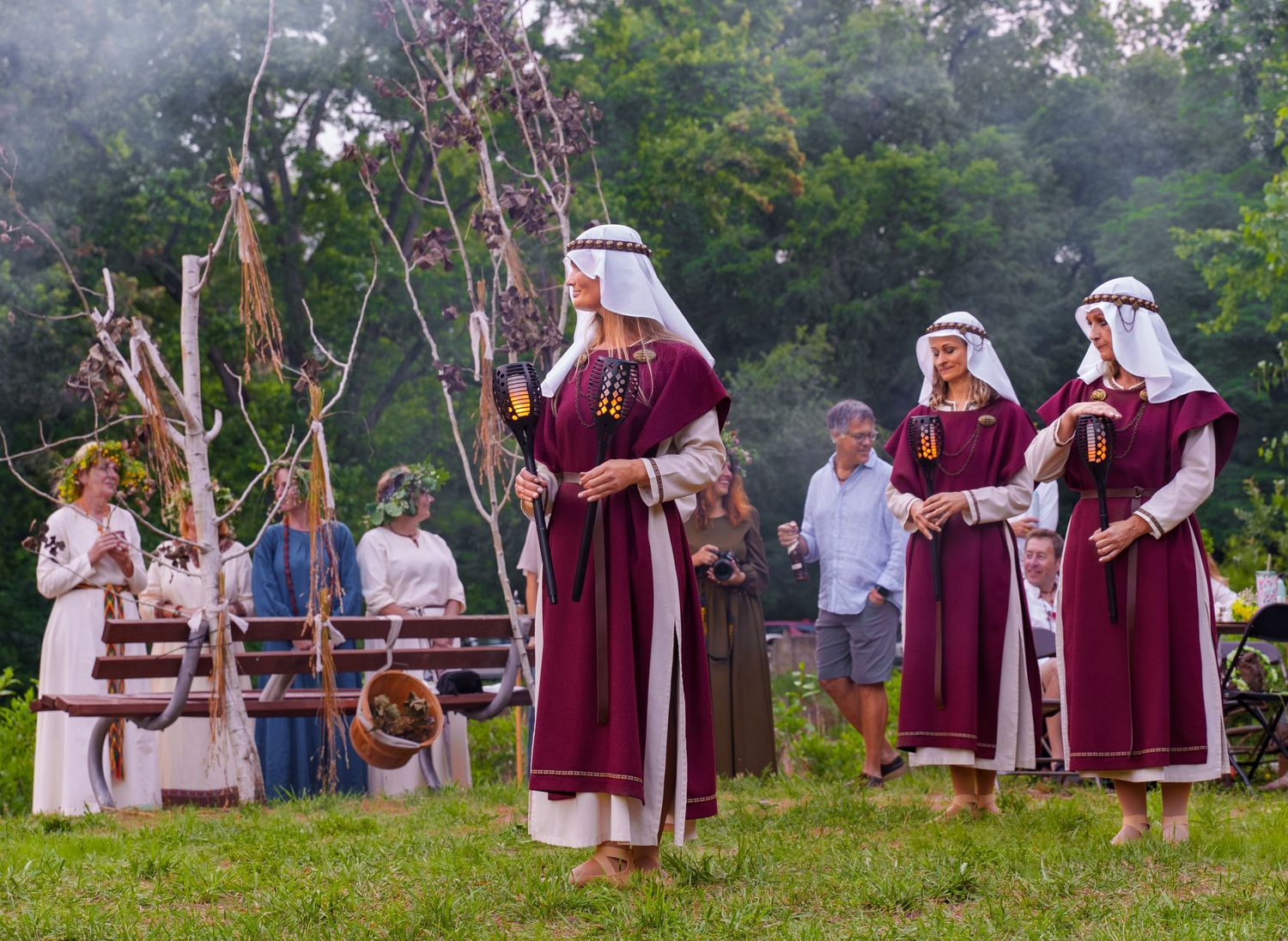 Women in traditional medieval burgundy costumes performing a midsummer ritual ceremony outdoors.