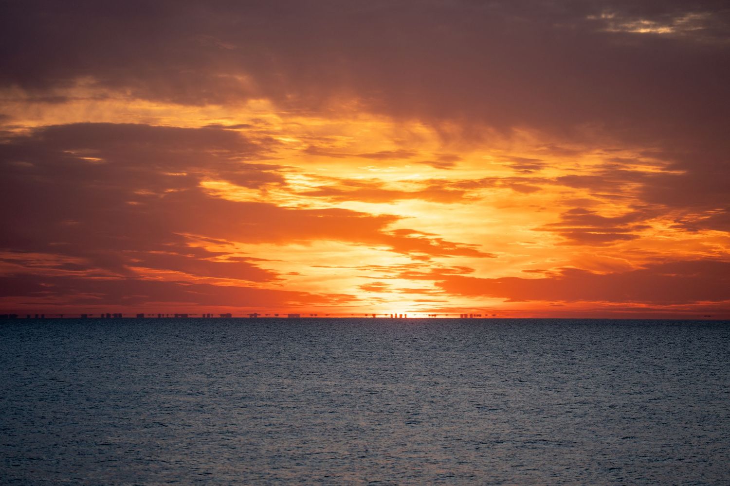 Vibrant orange and red sunset over calm ocean waters with dramatic cloudy sky reflecting warm golden hues.