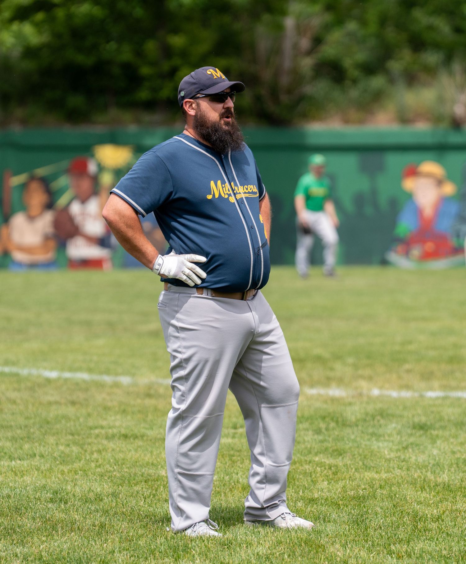 Bearded baseball player in blue jersey and gray pants stands on green field during a game.
