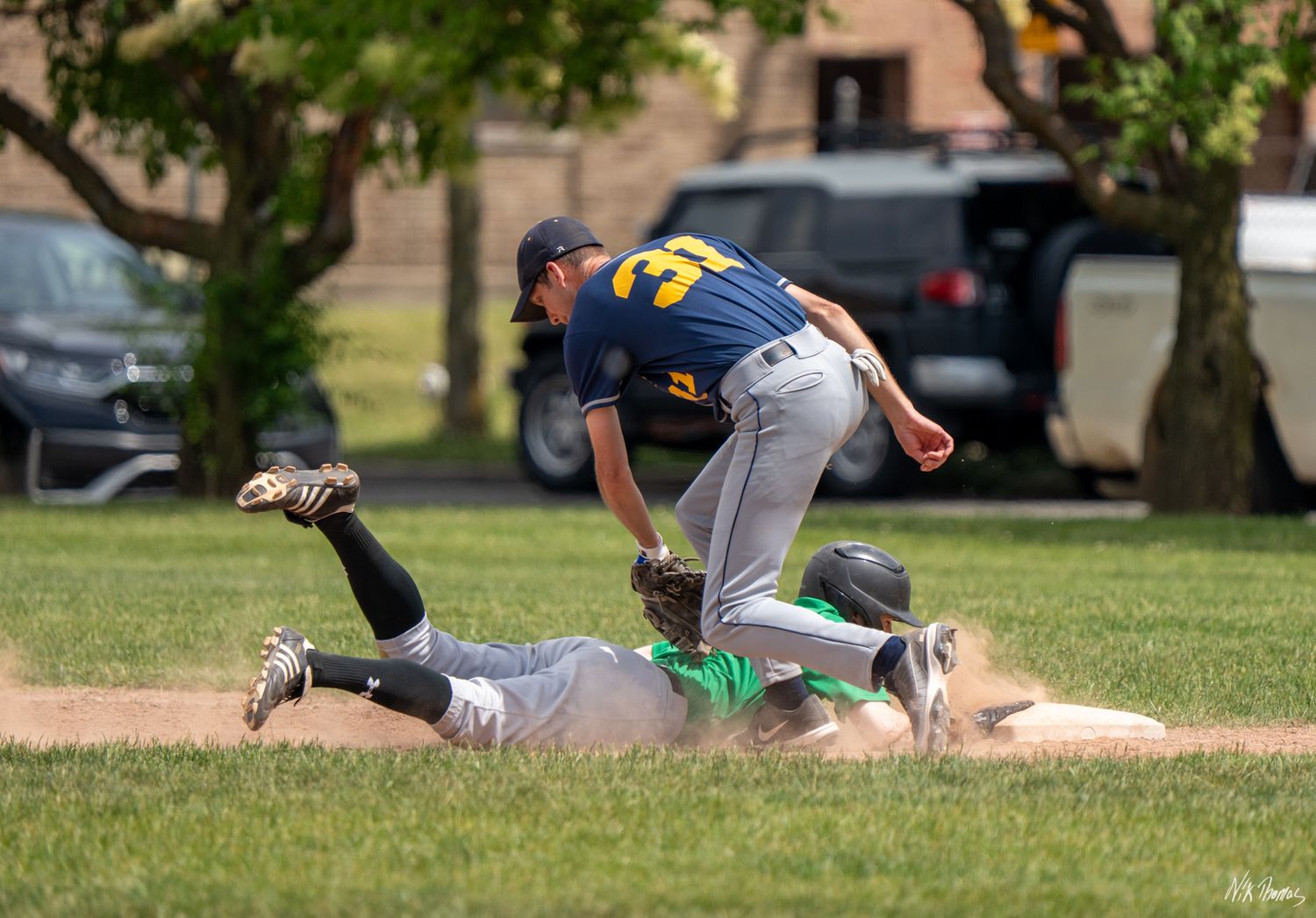 Baseball player sliding into base as fielder in navy jersey attempts tag during daytime game on grass field.