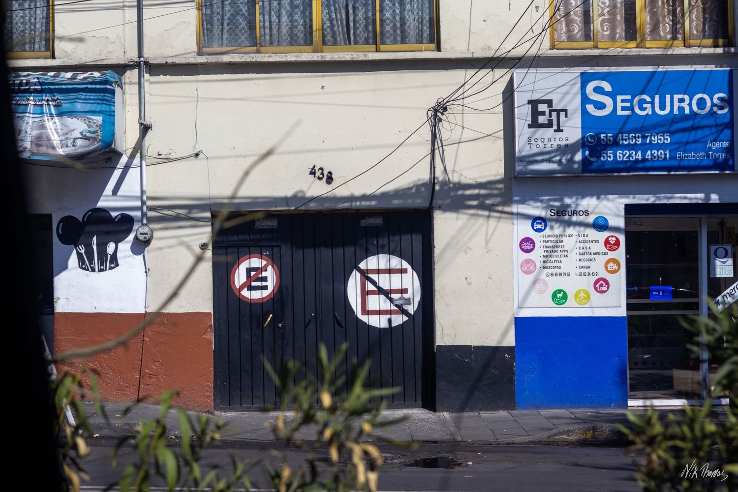 Mexican street storefront with no parking signs on black doors and Seguros insurance office.