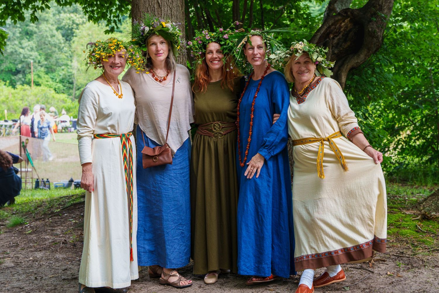 Five women in traditional folk costumes with flower crowns posing together at a midsummer festival.