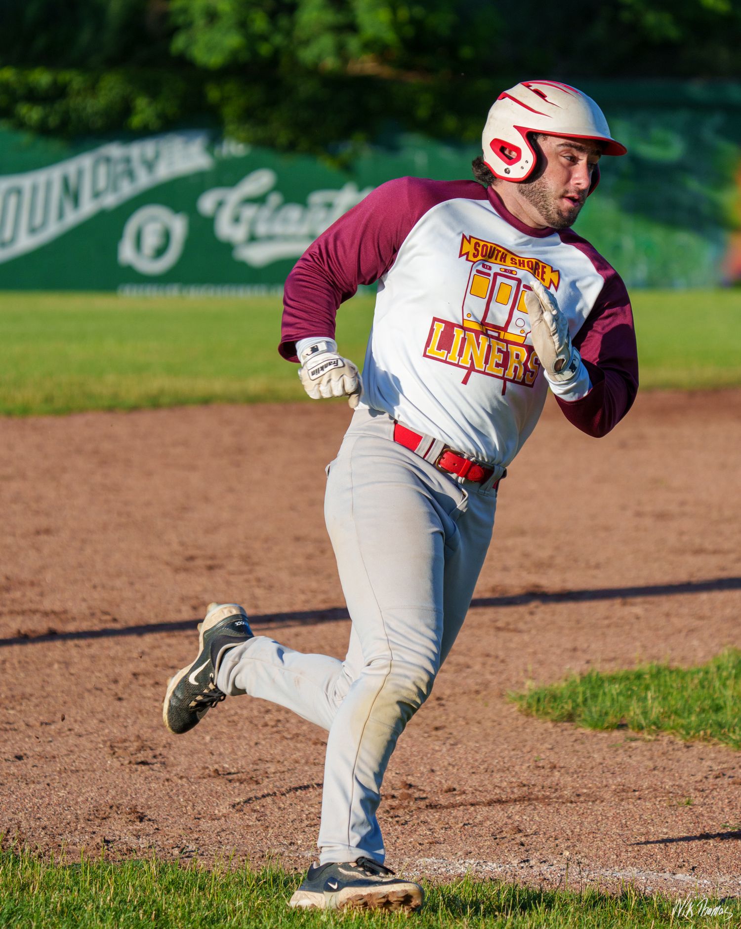 Baseball player in Liners uniform rounds third base during a game.
