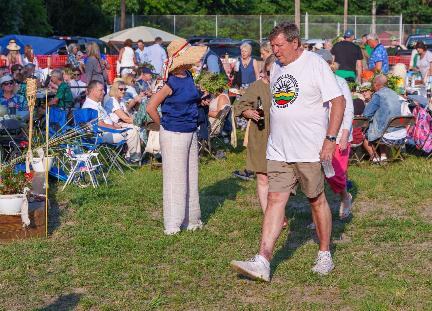 People socializing on a grassy field at an outdoor summer festival with crowds in the background.