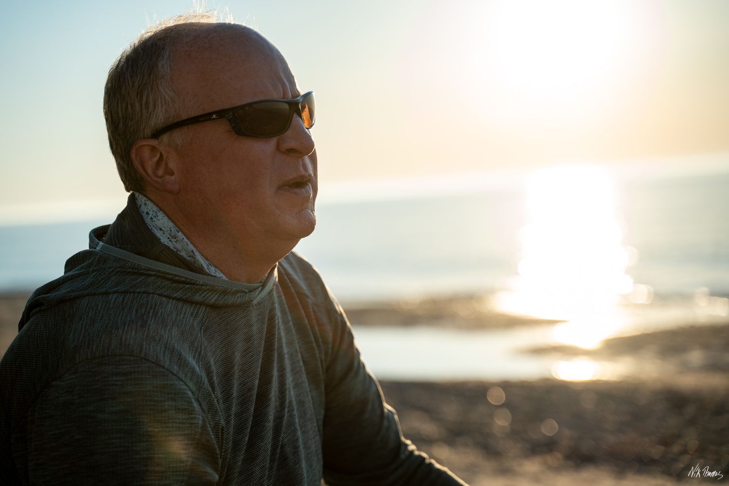 man staring at the sunset while sitting on the sand