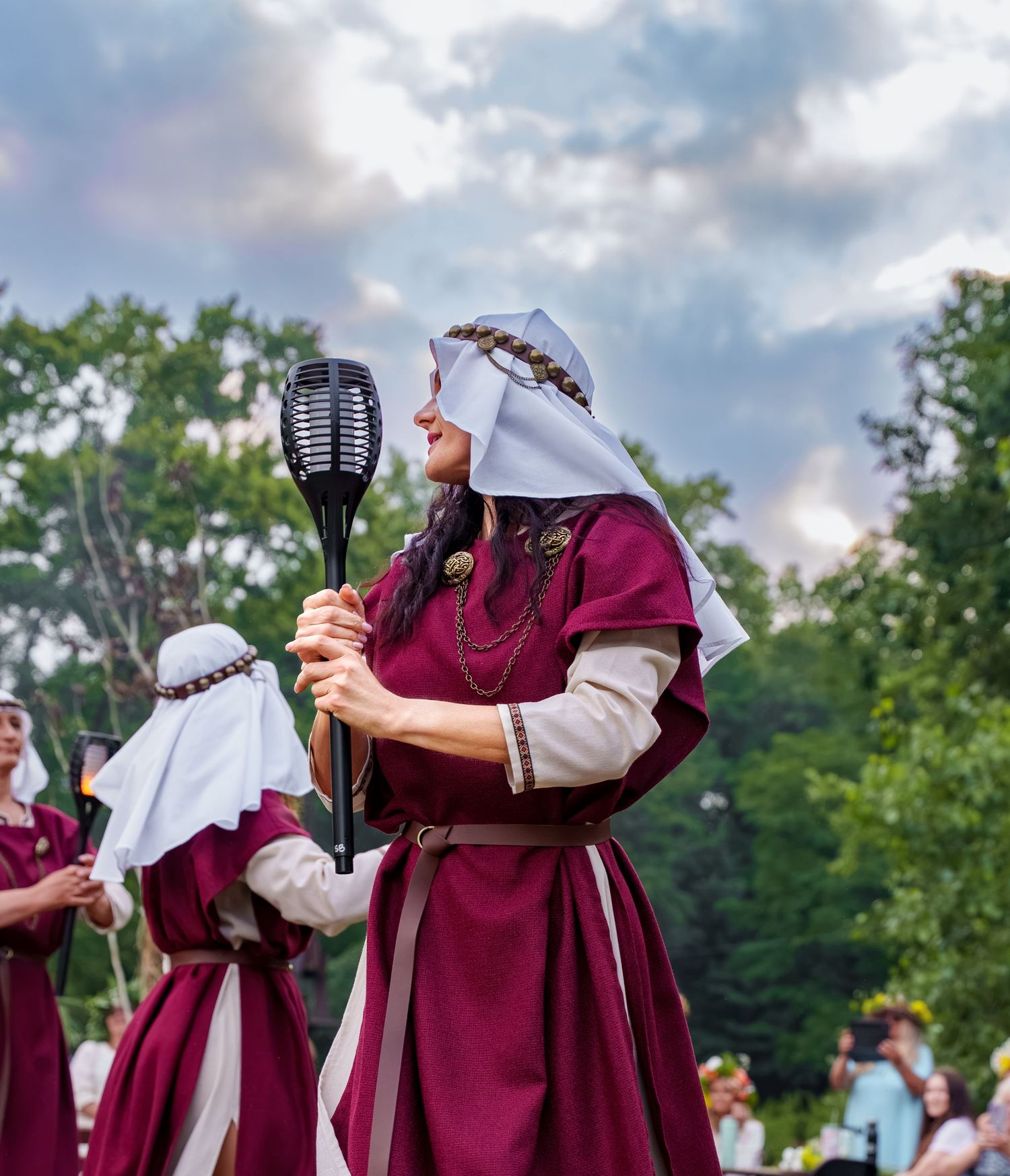 Woman in medieval burgundy dress holding a torch at a Renaissance festival outdoor event.