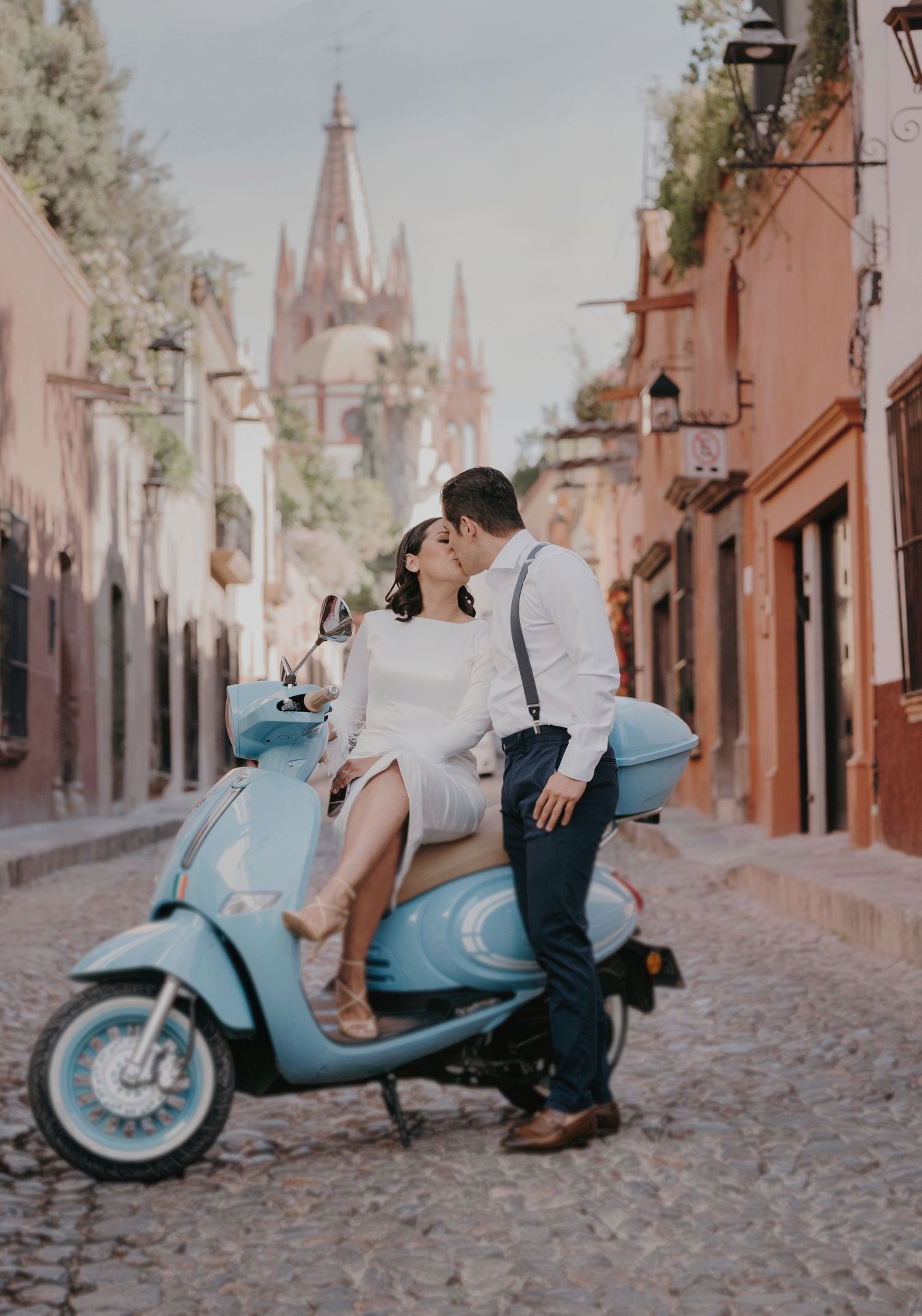 Couple kissing on a blue Vespa scooter on a cobblestone street in San Miguel de Allende, Mexico.
