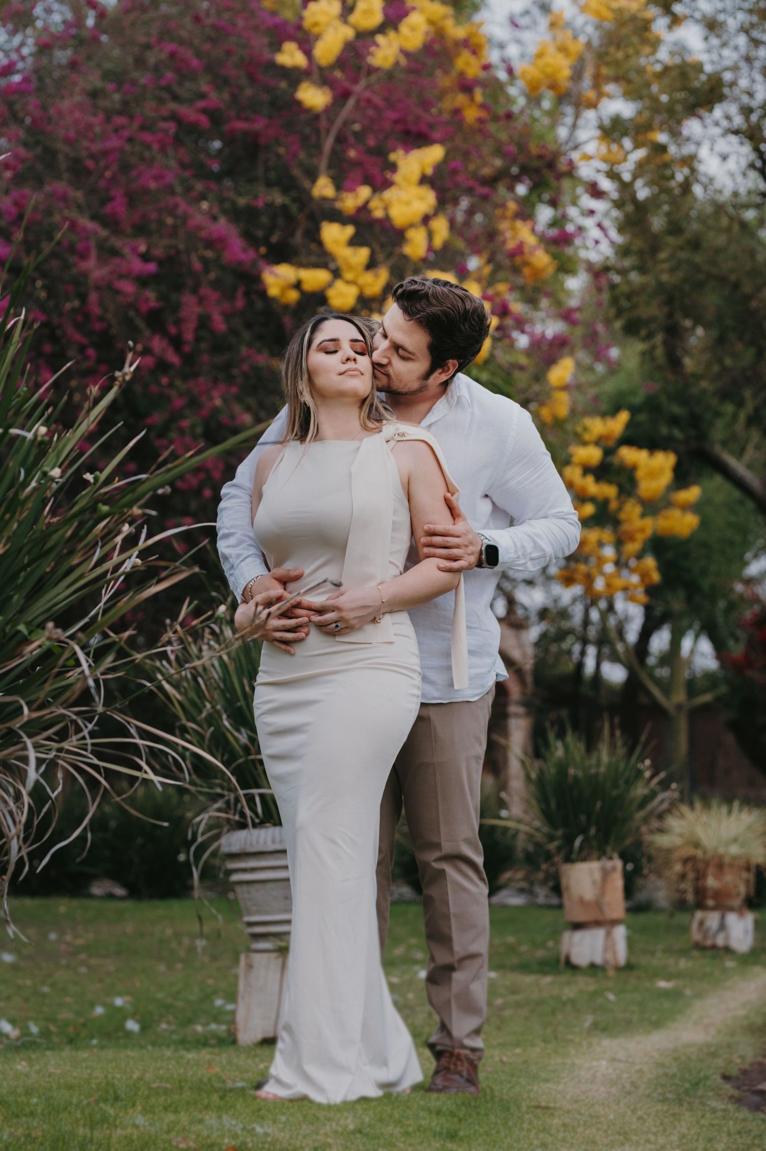 Romantic couple embracing in a lush garden surrounded by vibrant pink and yellow flowers.