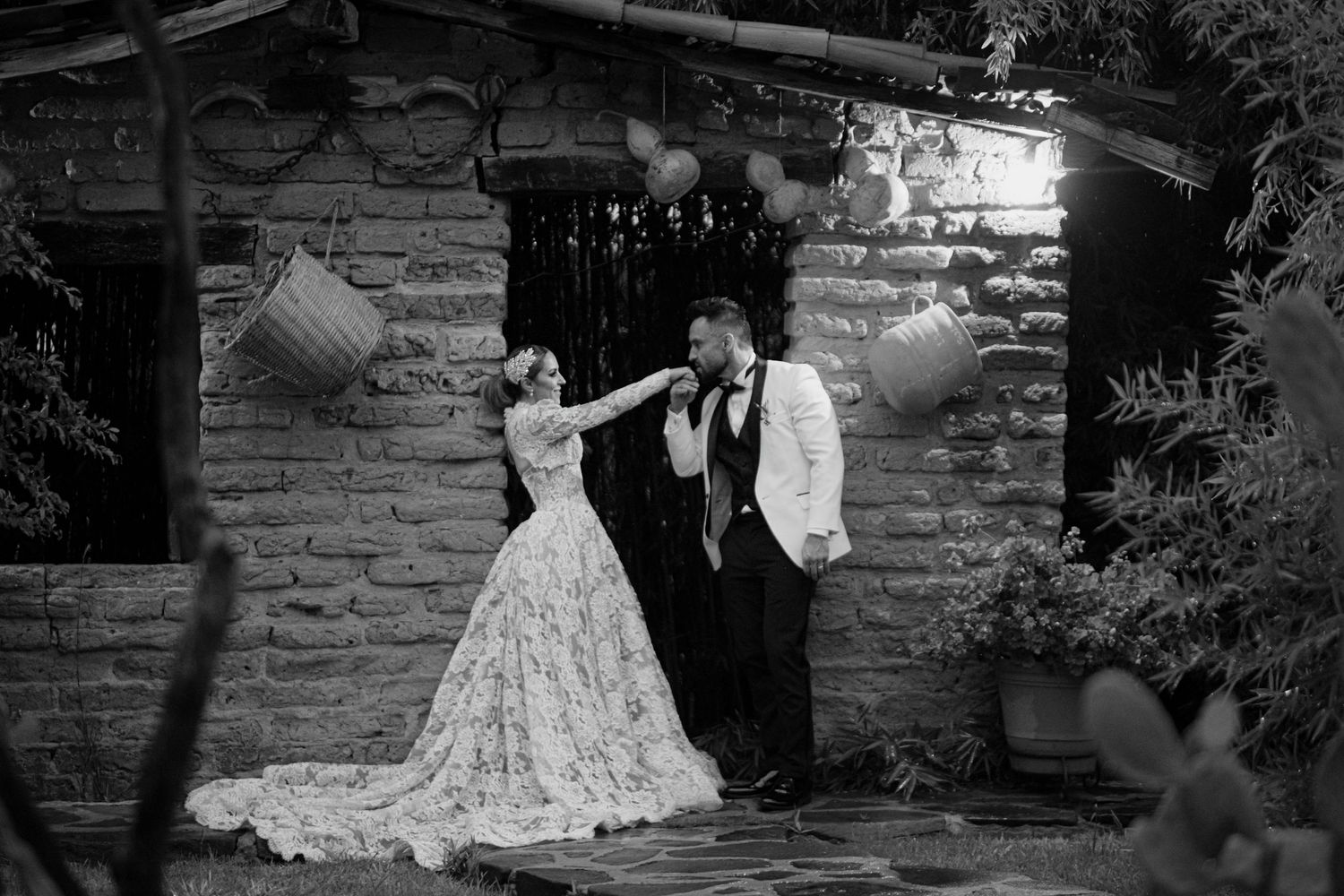 Black and white wedding photo of bride and groom dancing outside a rustic stone building surrounded by lush greenery.