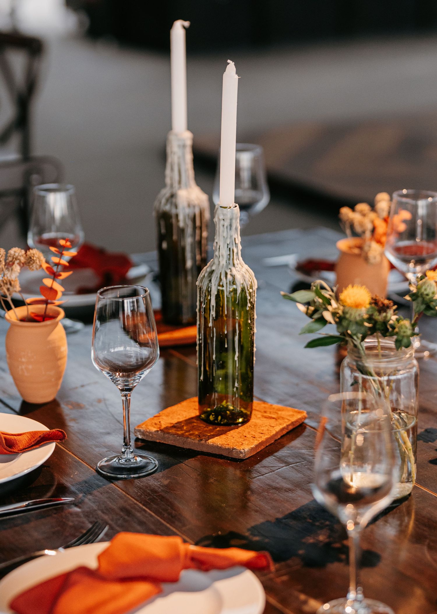 Rustic wedding table with candle in wine bottle, orange napkins and floral centerpieces.