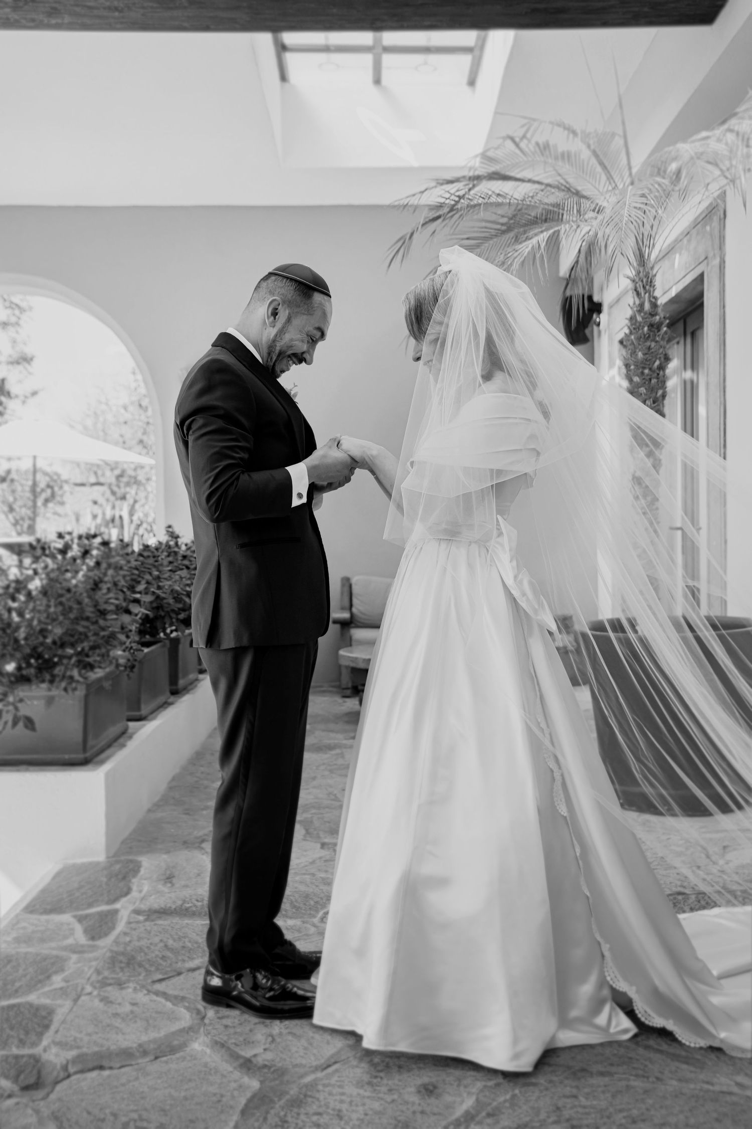 Black and white photo of a groom placing a ring on his bride's finger during an outdoor Jewish wedding ceremony.