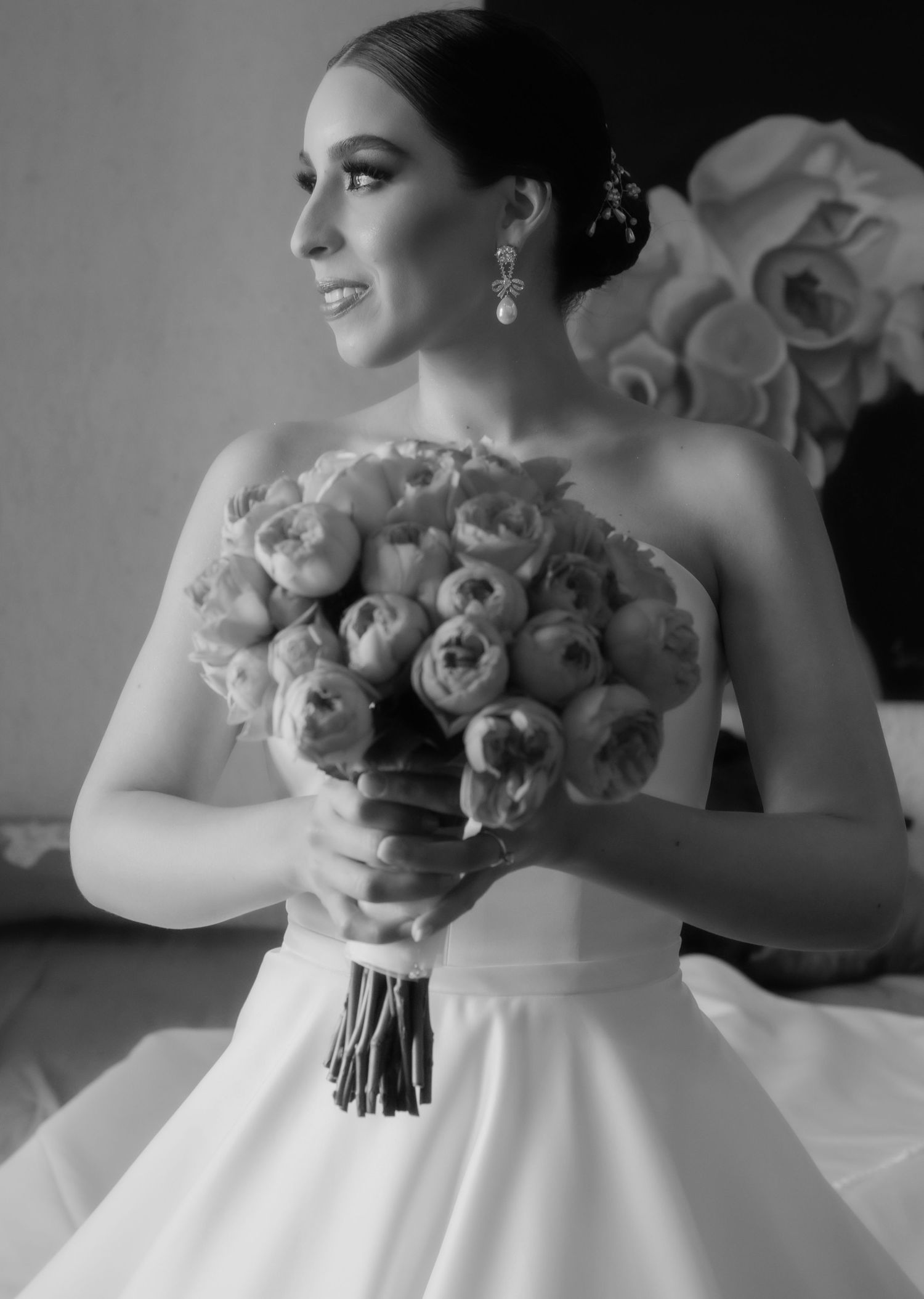 Elegant bride in strapless gown holding peony bouquet, black and white wedding portrait.