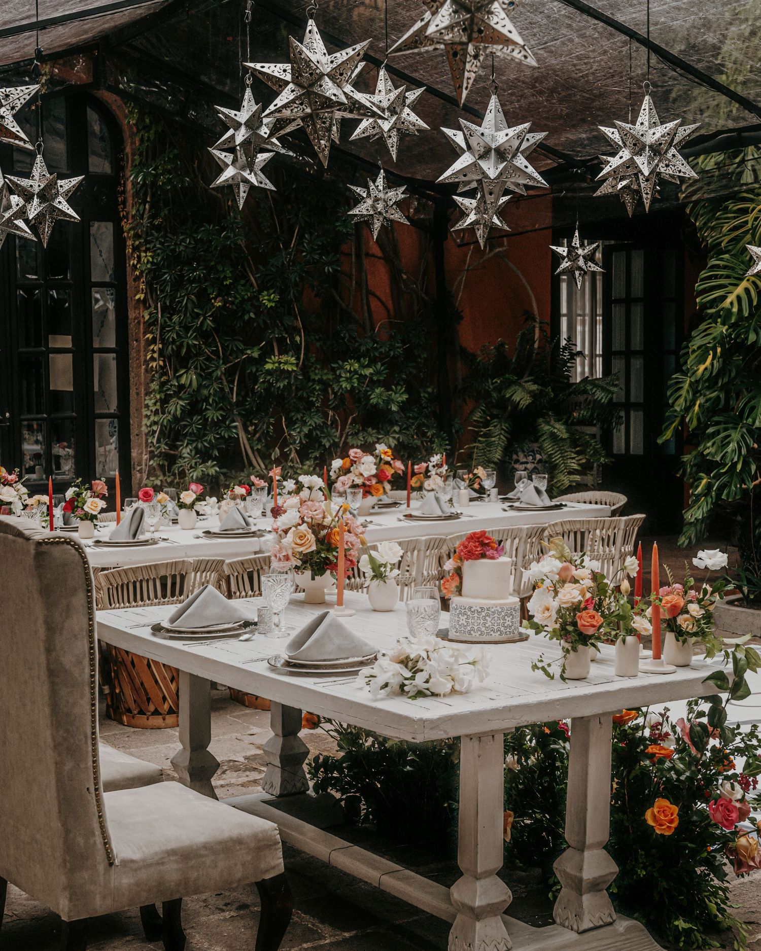 Elegant outdoor wedding reception table with star lanterns, colorful floral centerpieces, and lush greenery backdrop.