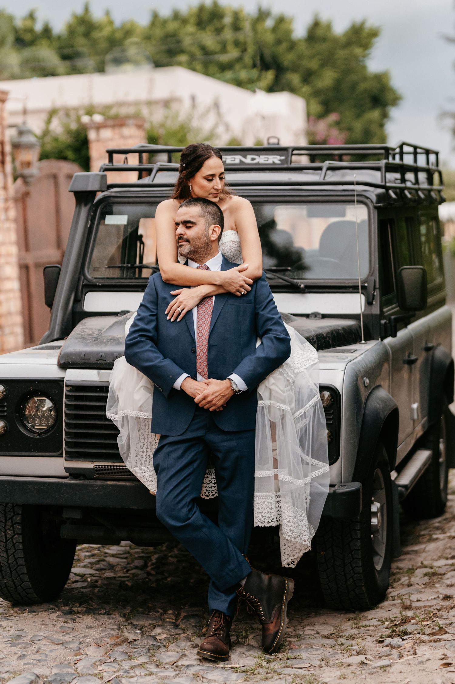 Bride and groom posing elegantly in front of a black Land Rover Defender on their wedding day.
