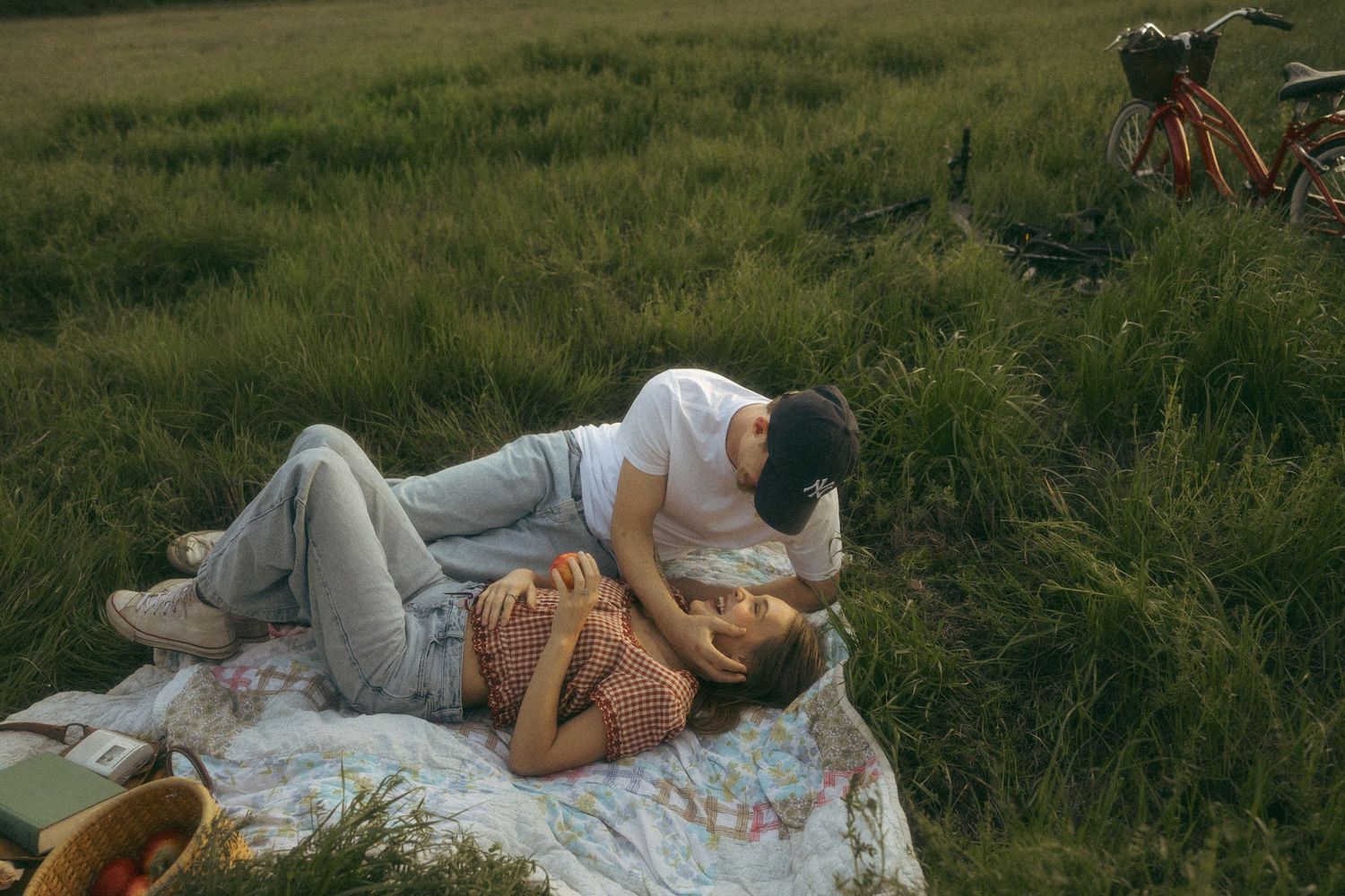 Couple relaxing together on a blanket in a lush green meadow with bicycles nearby.