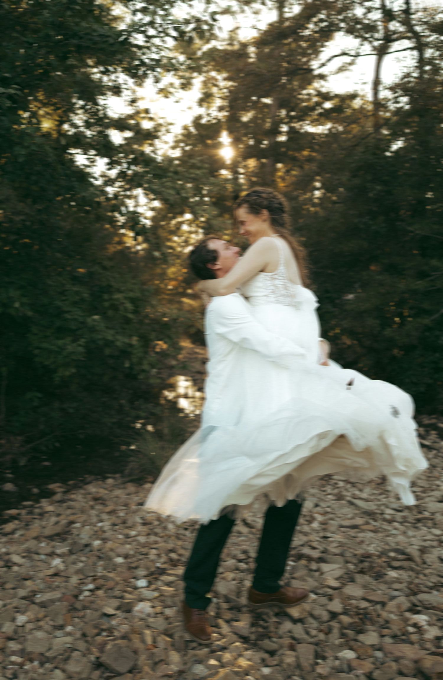 Groom lifting bride in white dress among autumn trees in a romantic outdoor wedding photo.