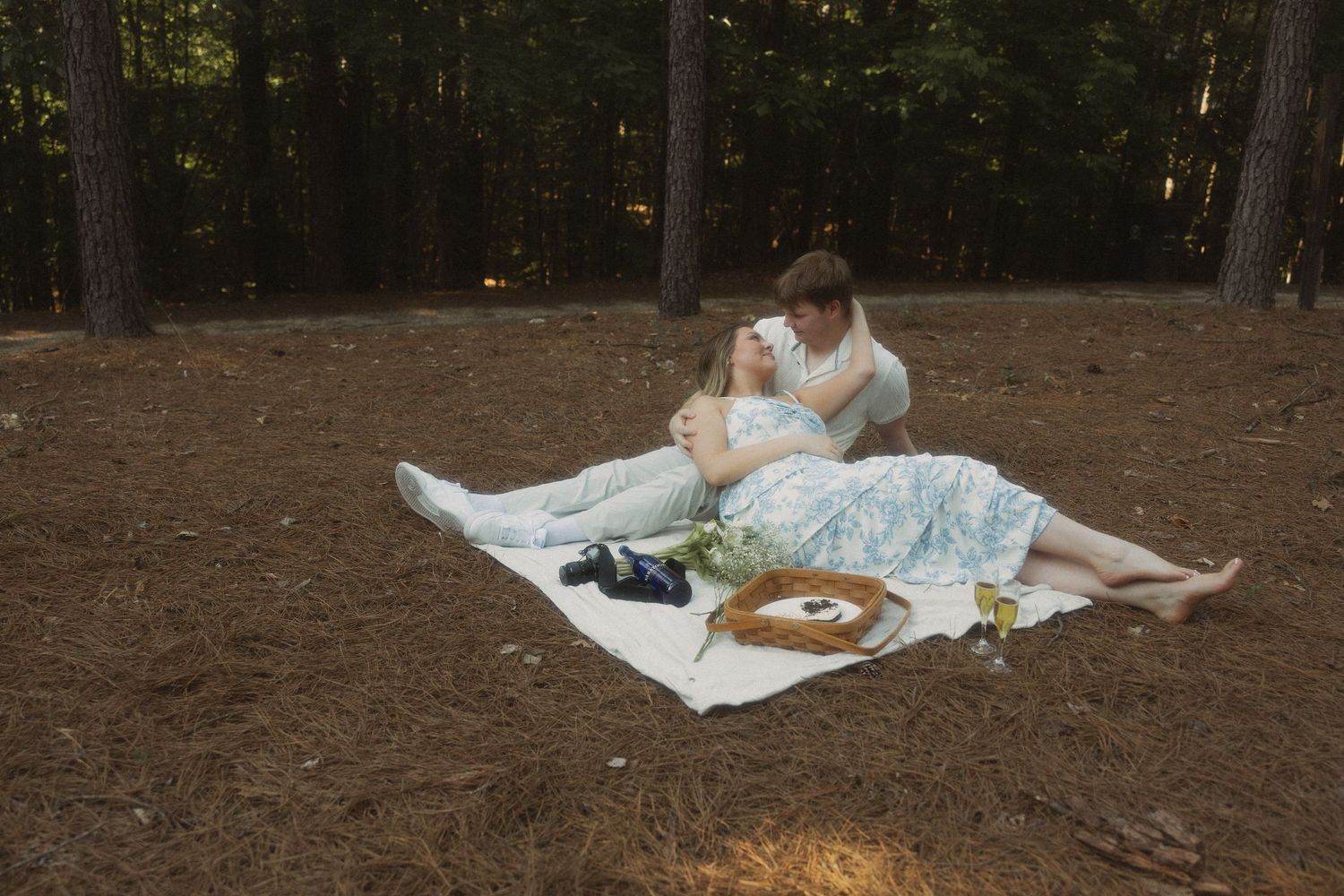 Couple relaxing on a blanket in a pine forest during a romantic picnic.