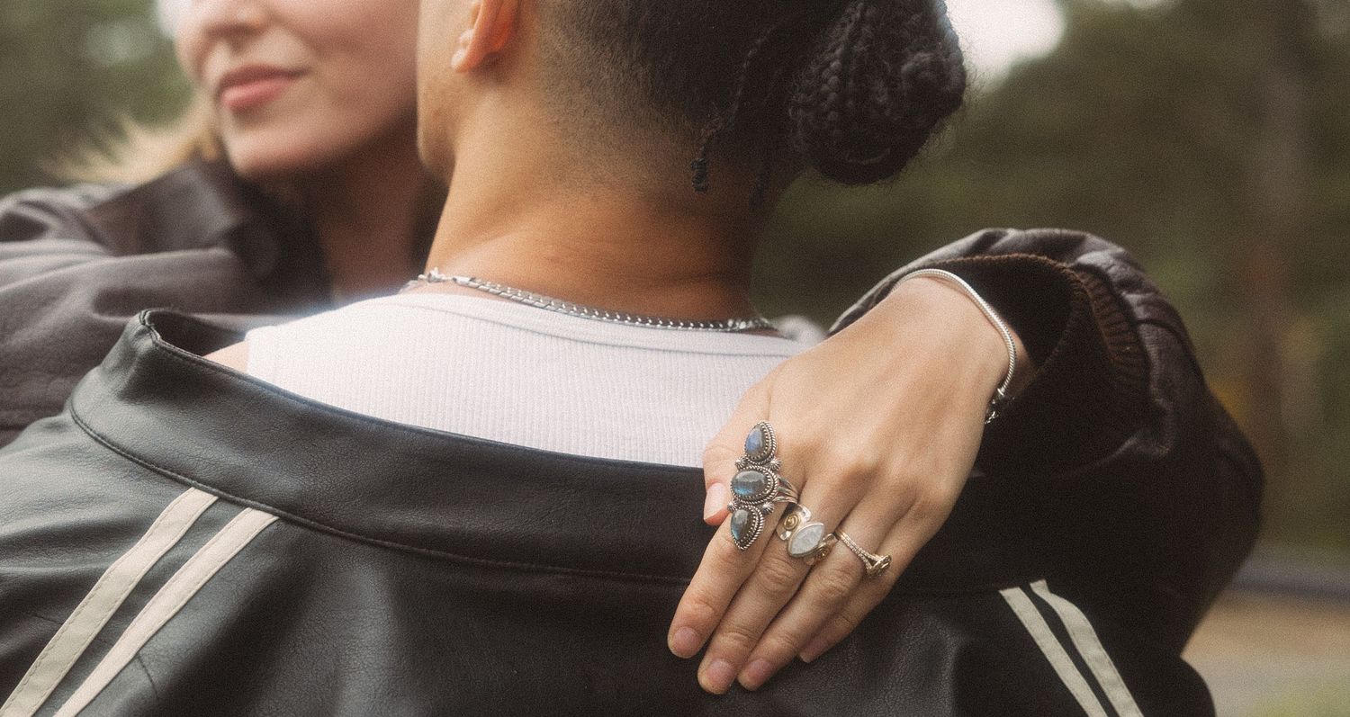 Close-up of a woman's hand adorned with silver rings resting on a partner's leather jacket shoulder.