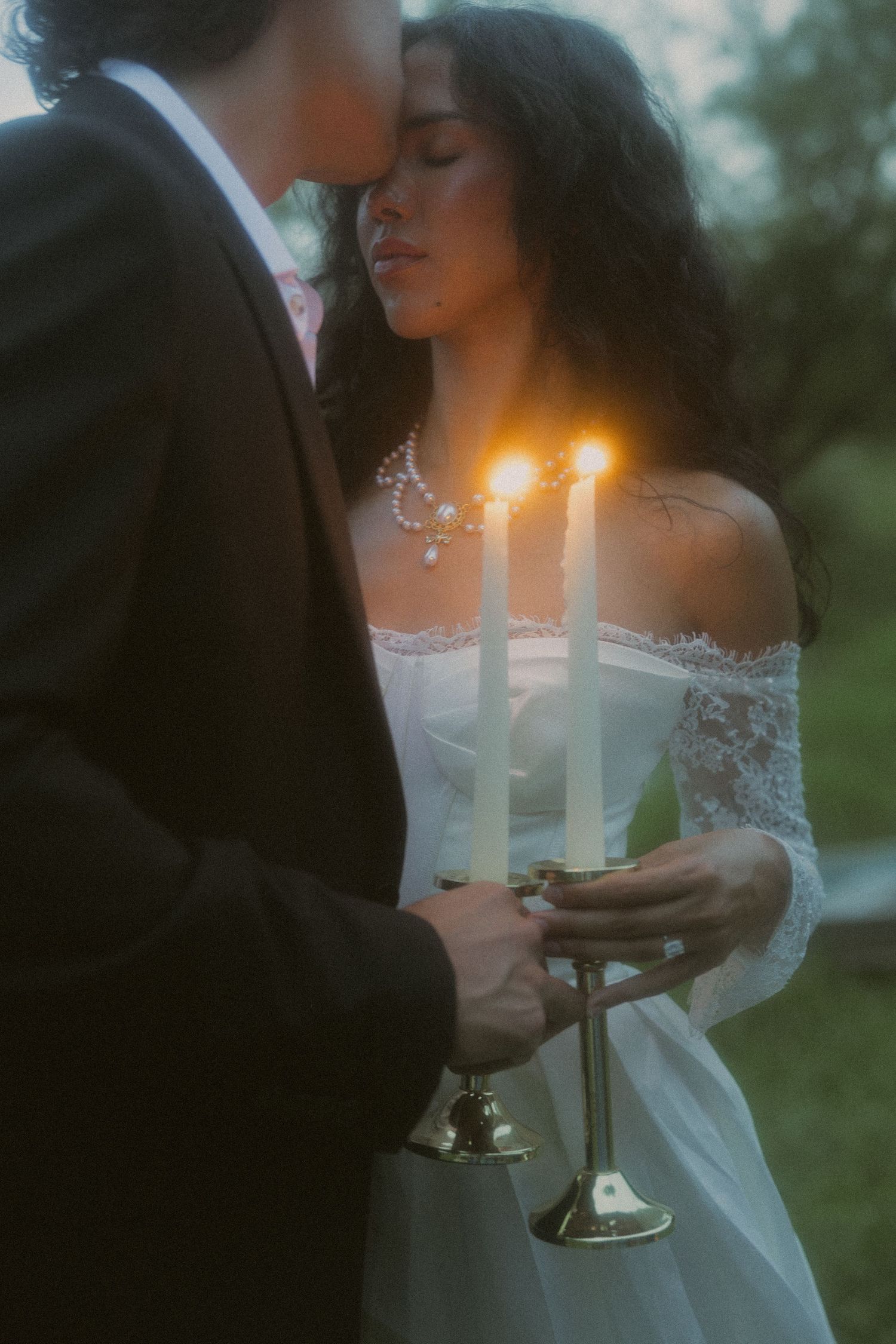 A bride in lace gown holds lit candles with her partner in a romantic twilight ceremony.