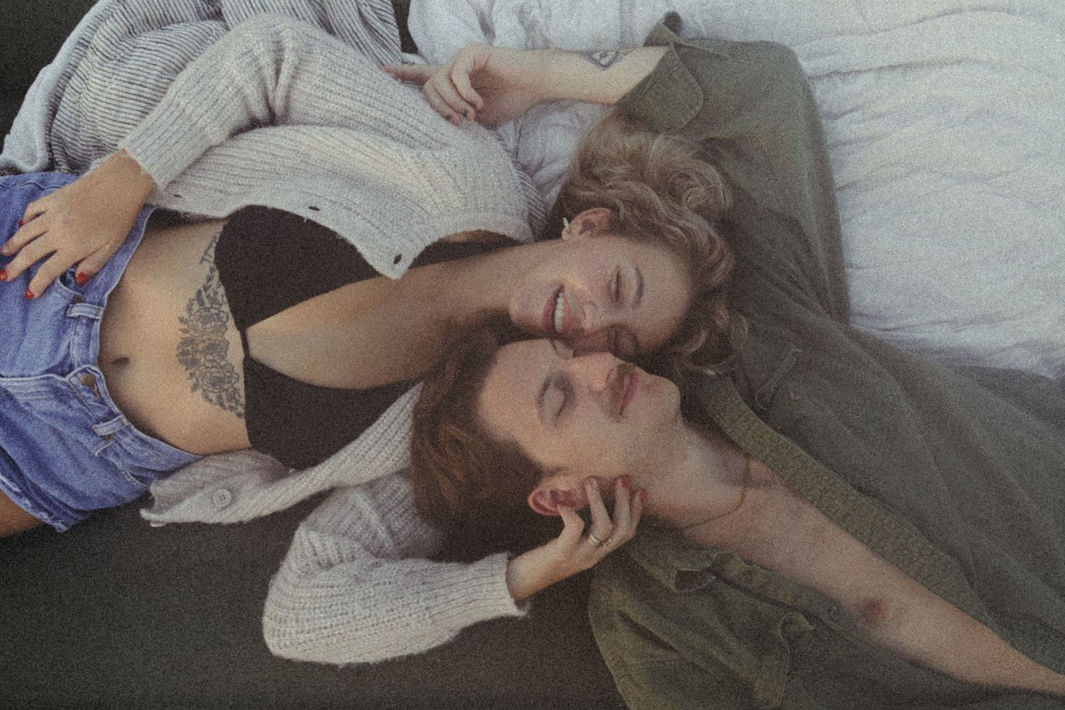 Two women lying close together on a bed in cozy sweaters in an intimate portrait.