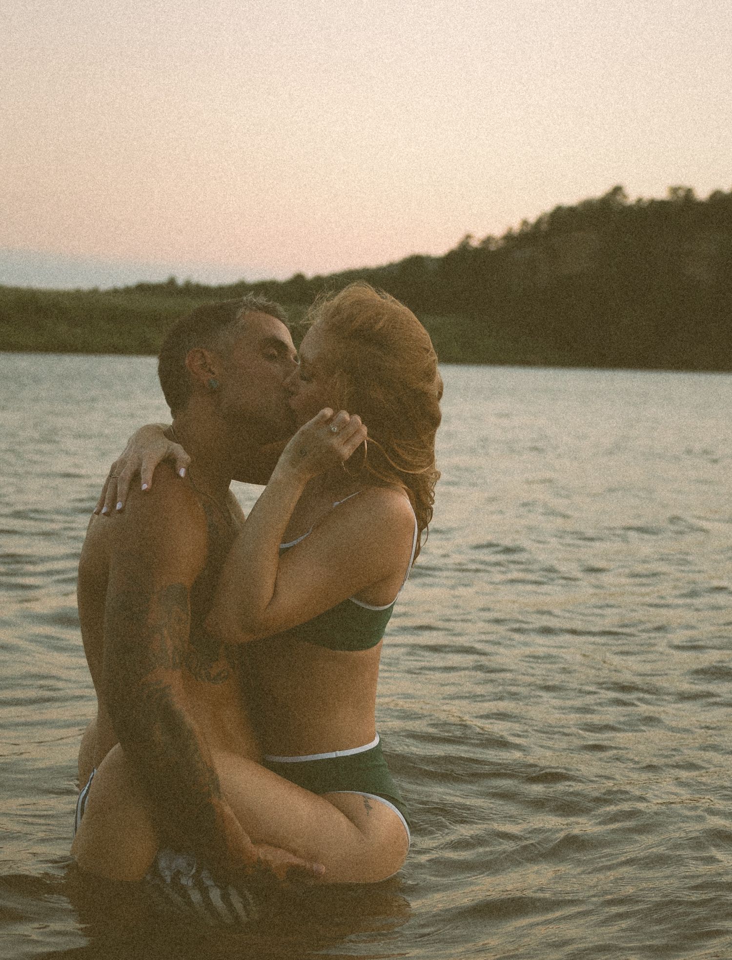 Couple sharing a passionate kiss while standing in a lake at golden sunset.