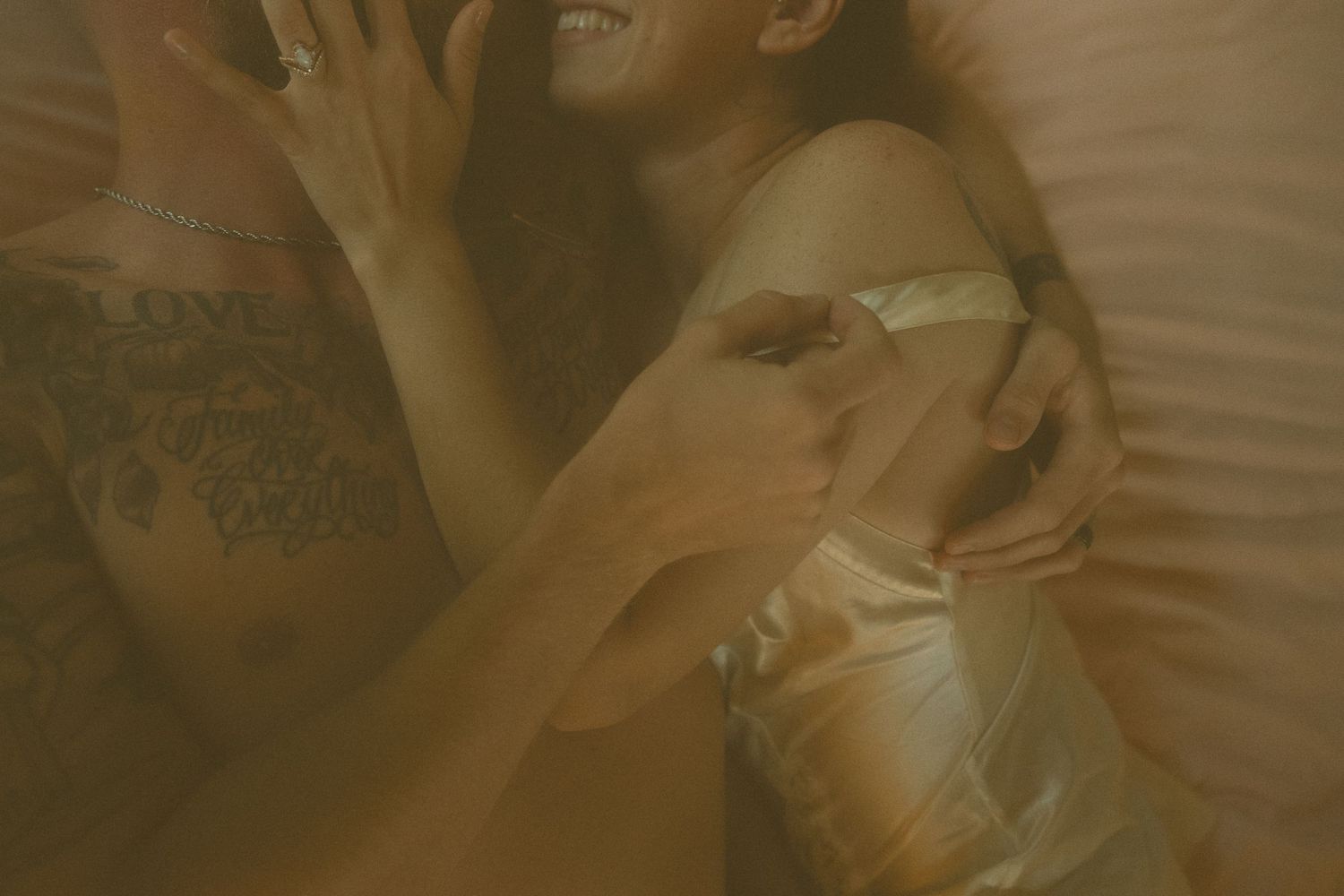 Intimate couple sharing a playful moment in bed with warm golden lighting.