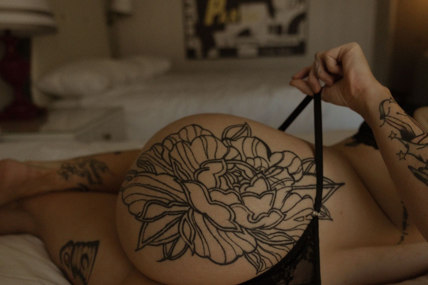 Person lying face down on bed showcasing large floral tattoo on back with black lingerie.