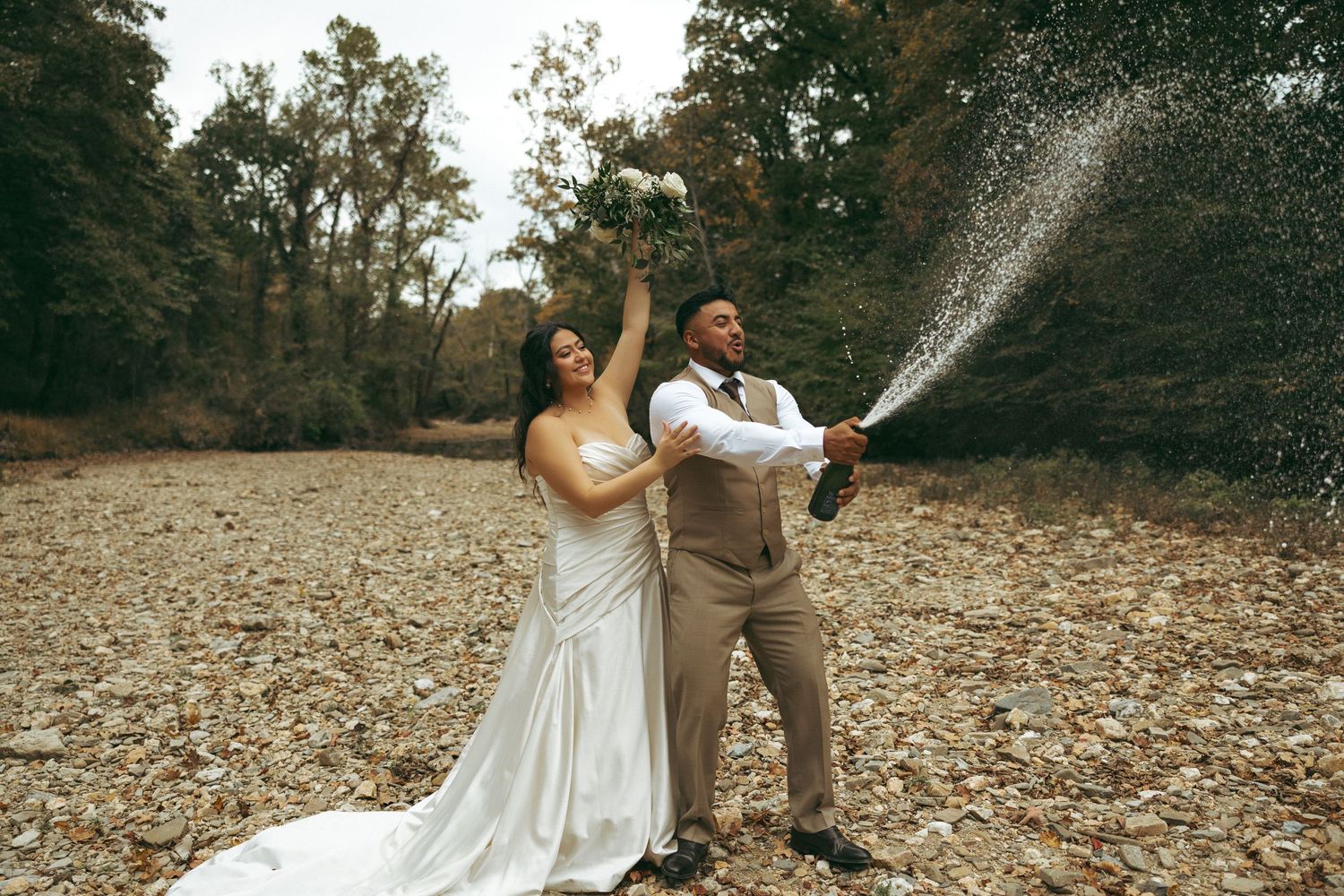 Joyful newlyweds spraying champagne outdoors surrounded by autumn foliage.