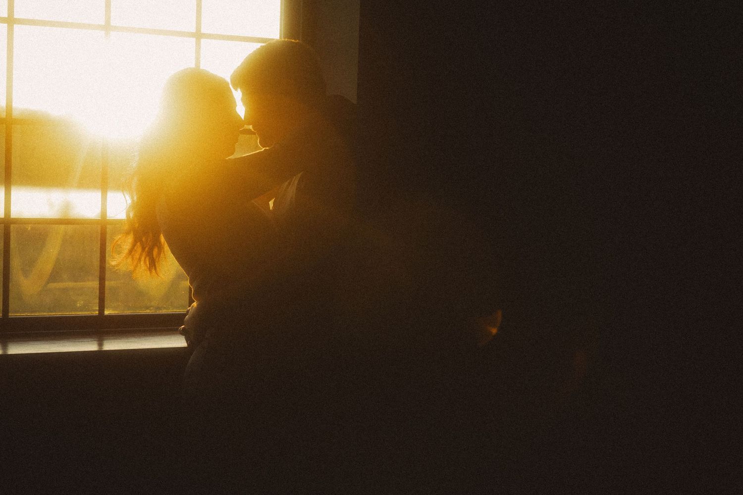 Romantic couple silhouetted against a stunning golden sunset by a window.