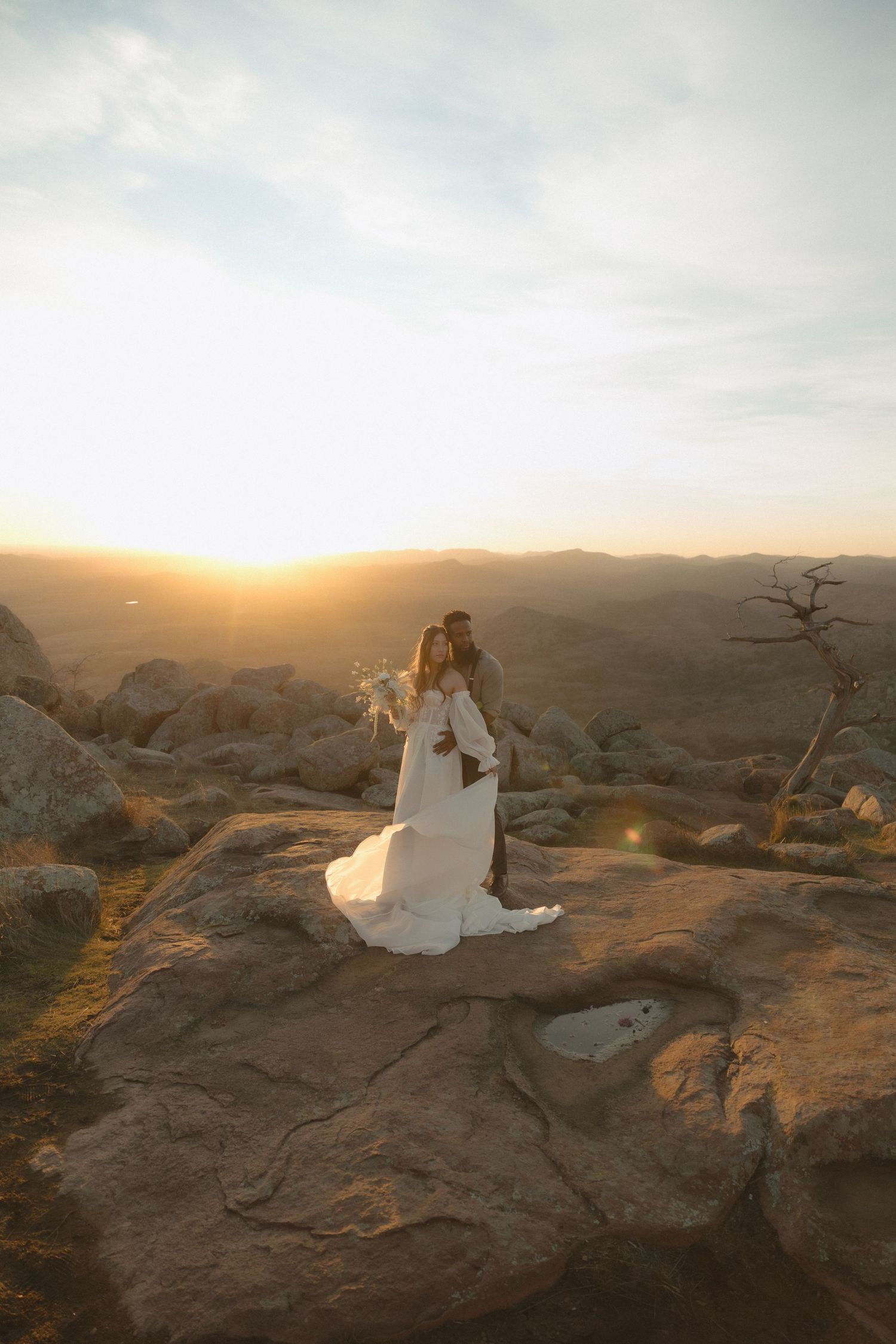 Bride and groom embracing on rocky desert landscape during a golden sunset elopement.