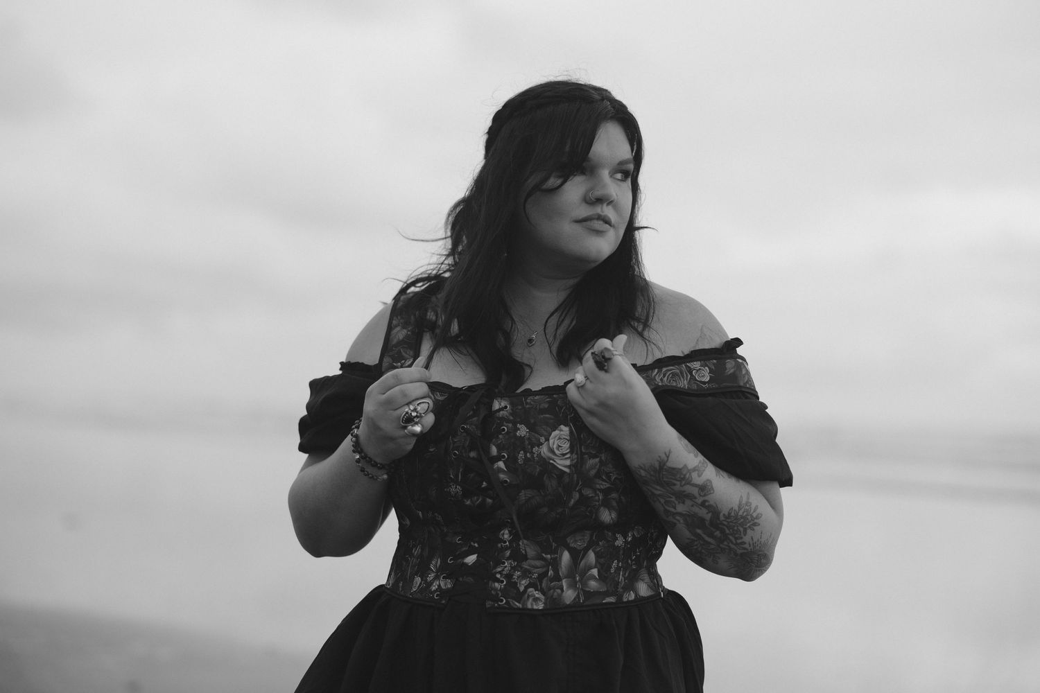 Black and white portrait of a woman in an off-shoulder dress outdoors.