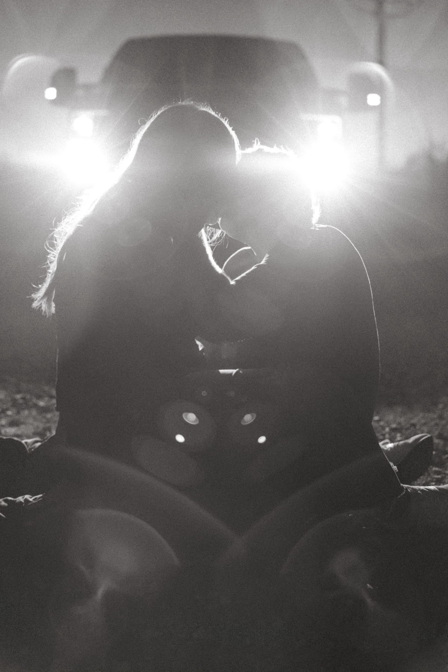Romantic black and white silhouette of a couple kissing in bright truck headlights.