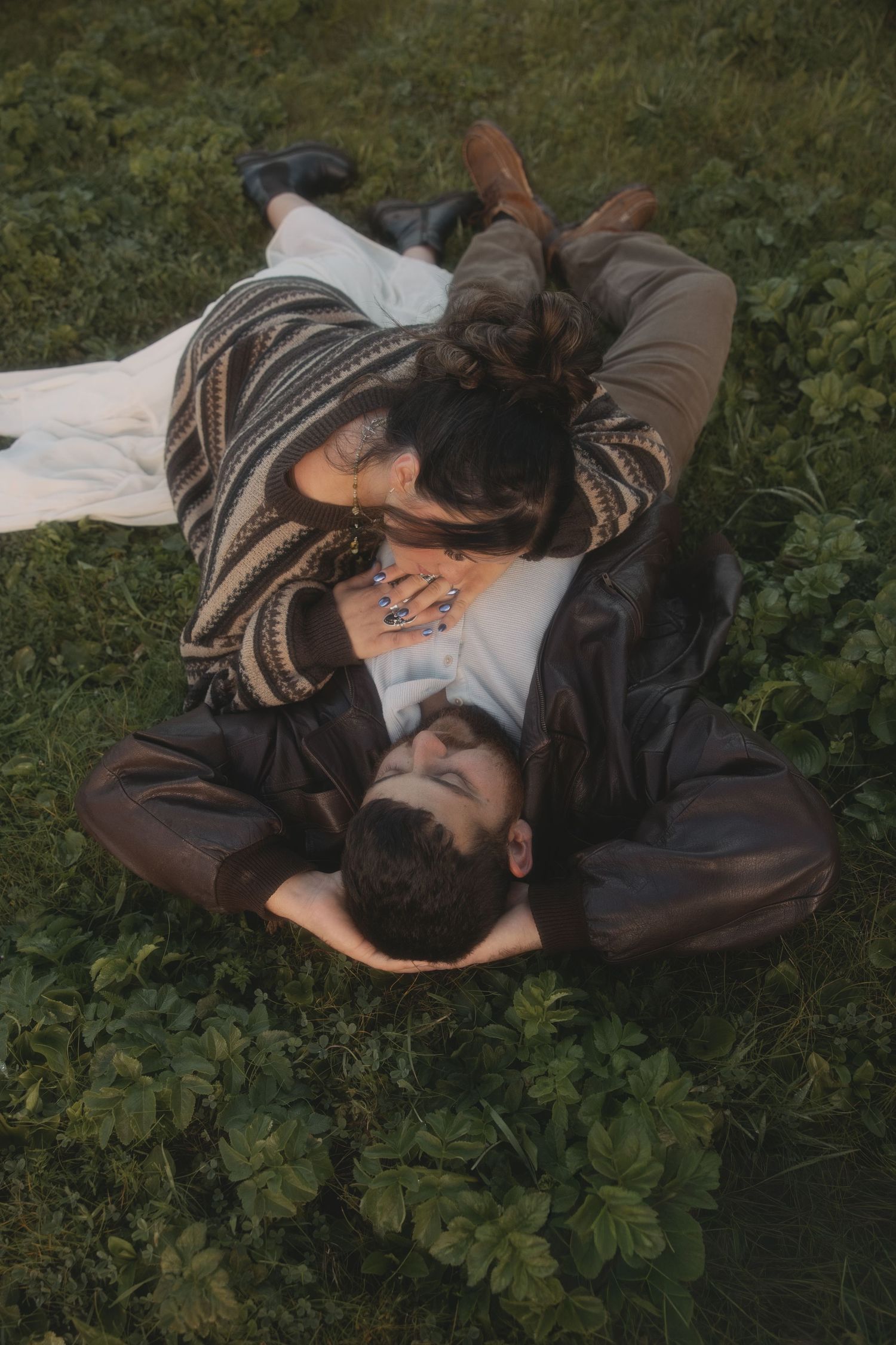 Couple lying on green grass sharing a tender kiss in a romantic outdoor setting.
