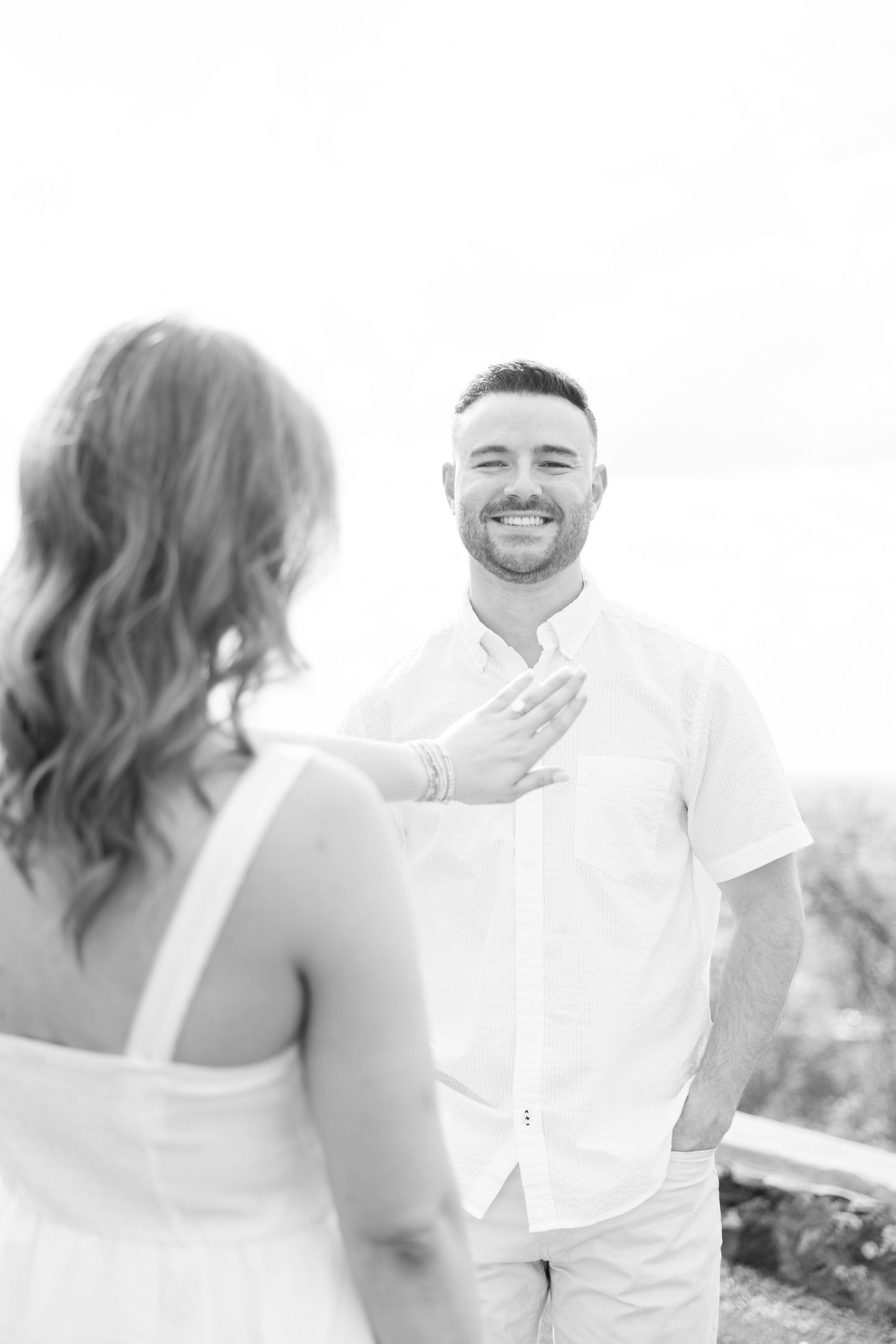 Smiling groom in white shirt reacts emotionally during first look with bride at outdoor wedding venue.
