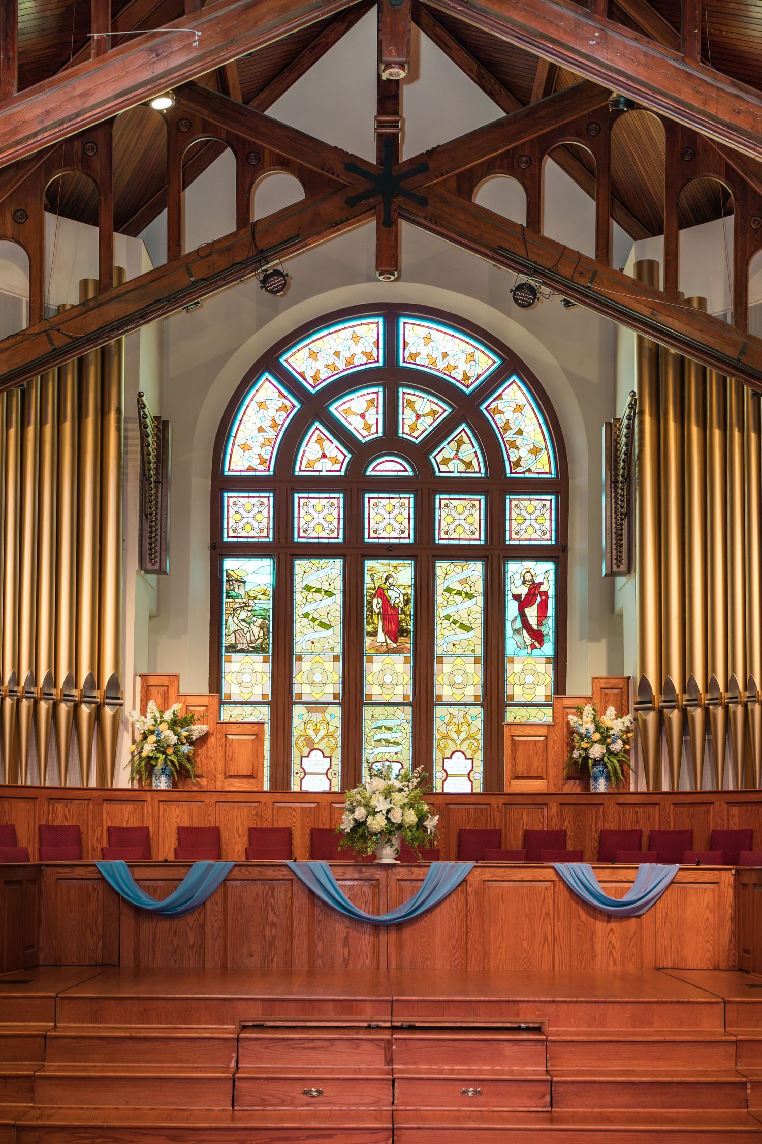 Beautiful church altar with stained glass window, pipe organ, and floral wedding decorations.