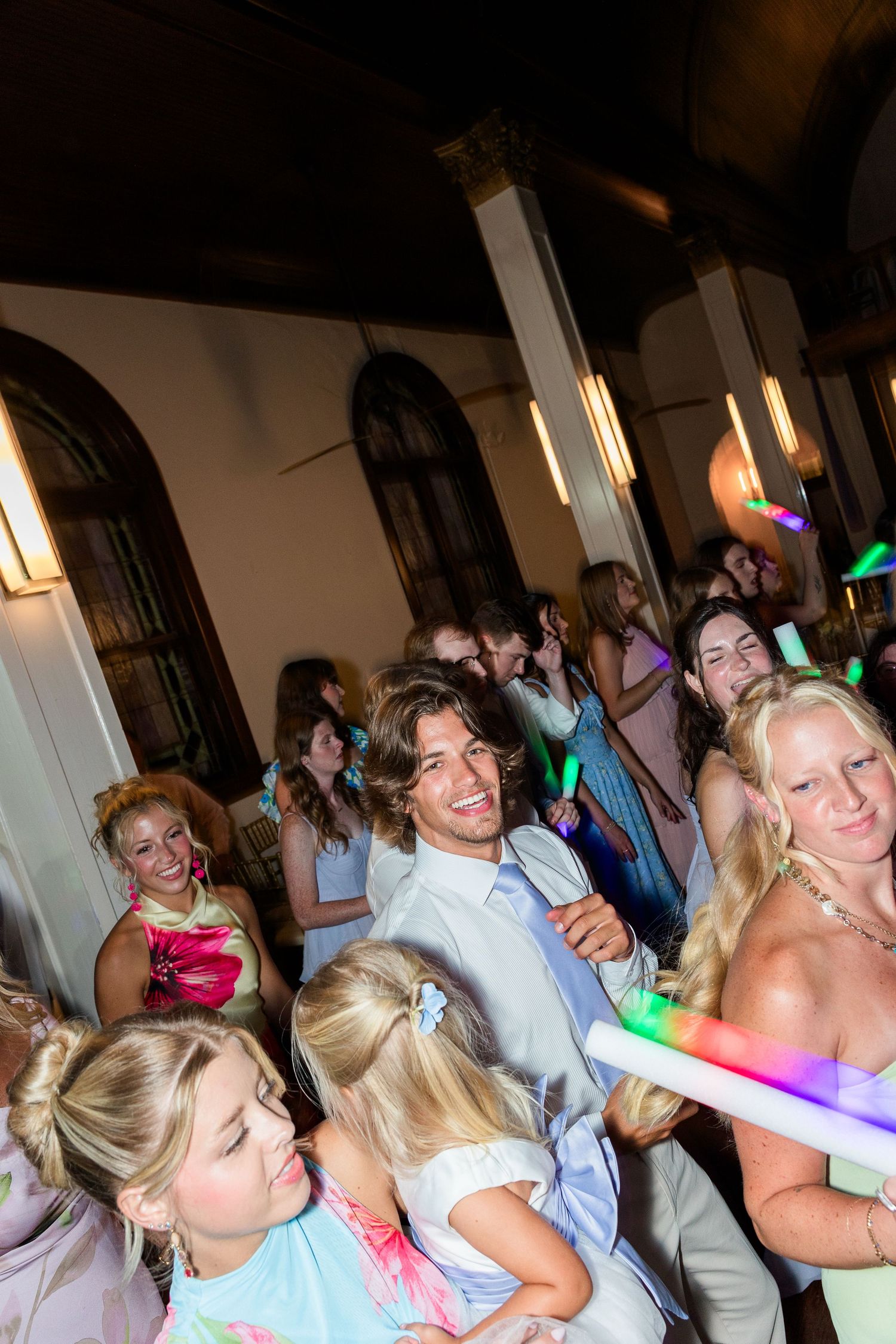 Joyful wedding reception dance floor with guests holding glowing foam sticks celebrating with the groom.