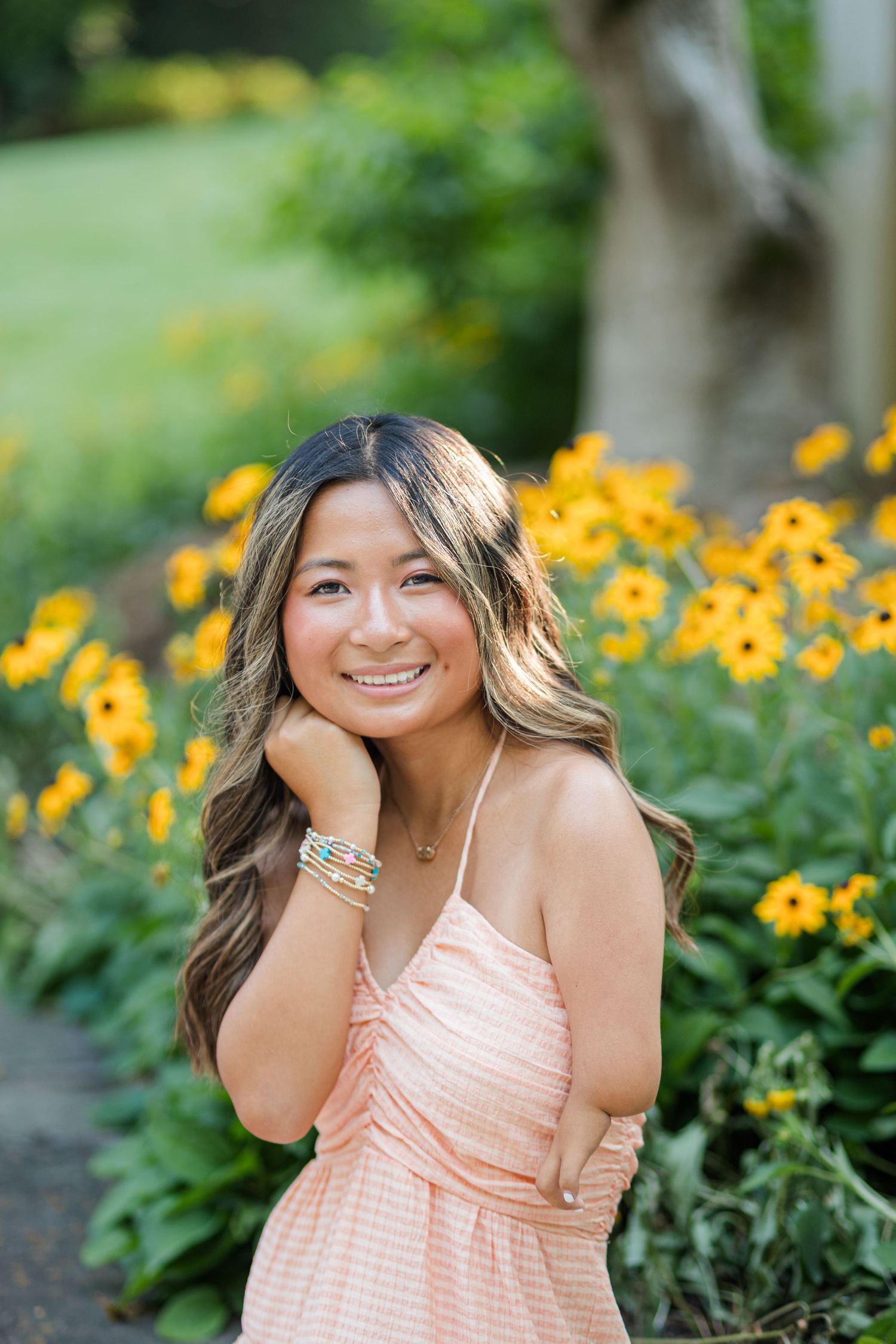 A cheerful young woman in a peach dress smiles beside bright yellow black-eyed Susan flowers.