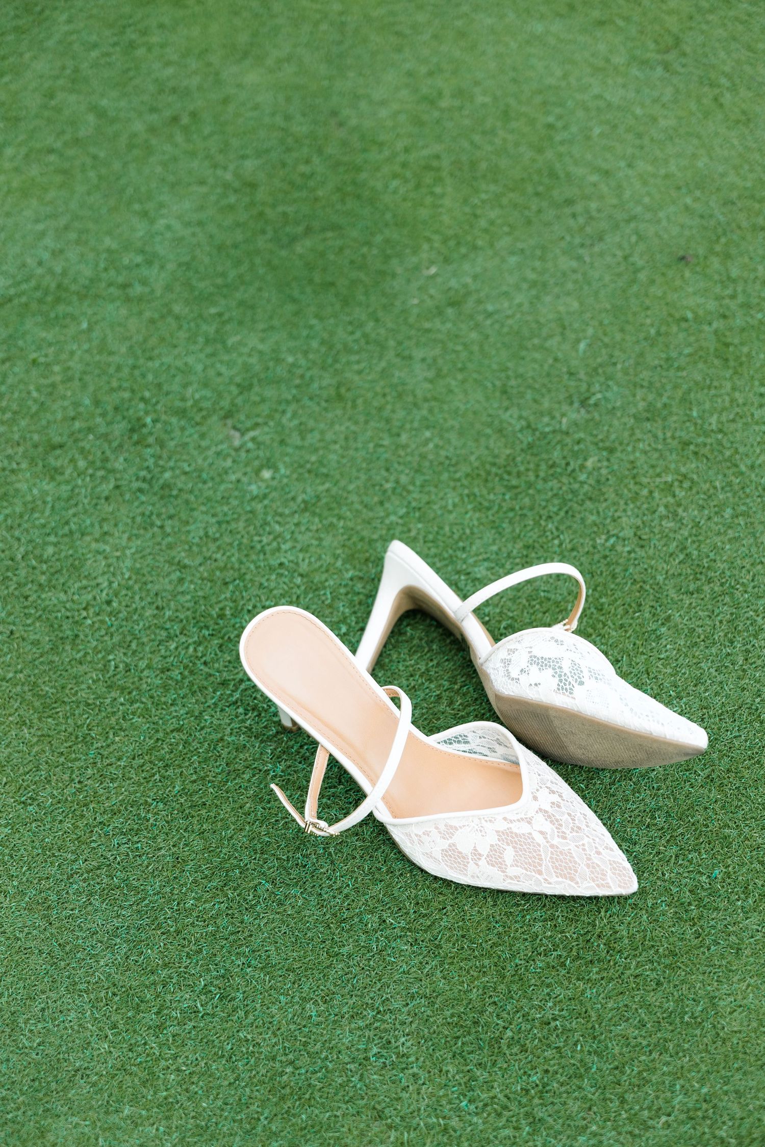 Elegant white lace pointed-toe mule heels with kitten heel on green grass lawn.