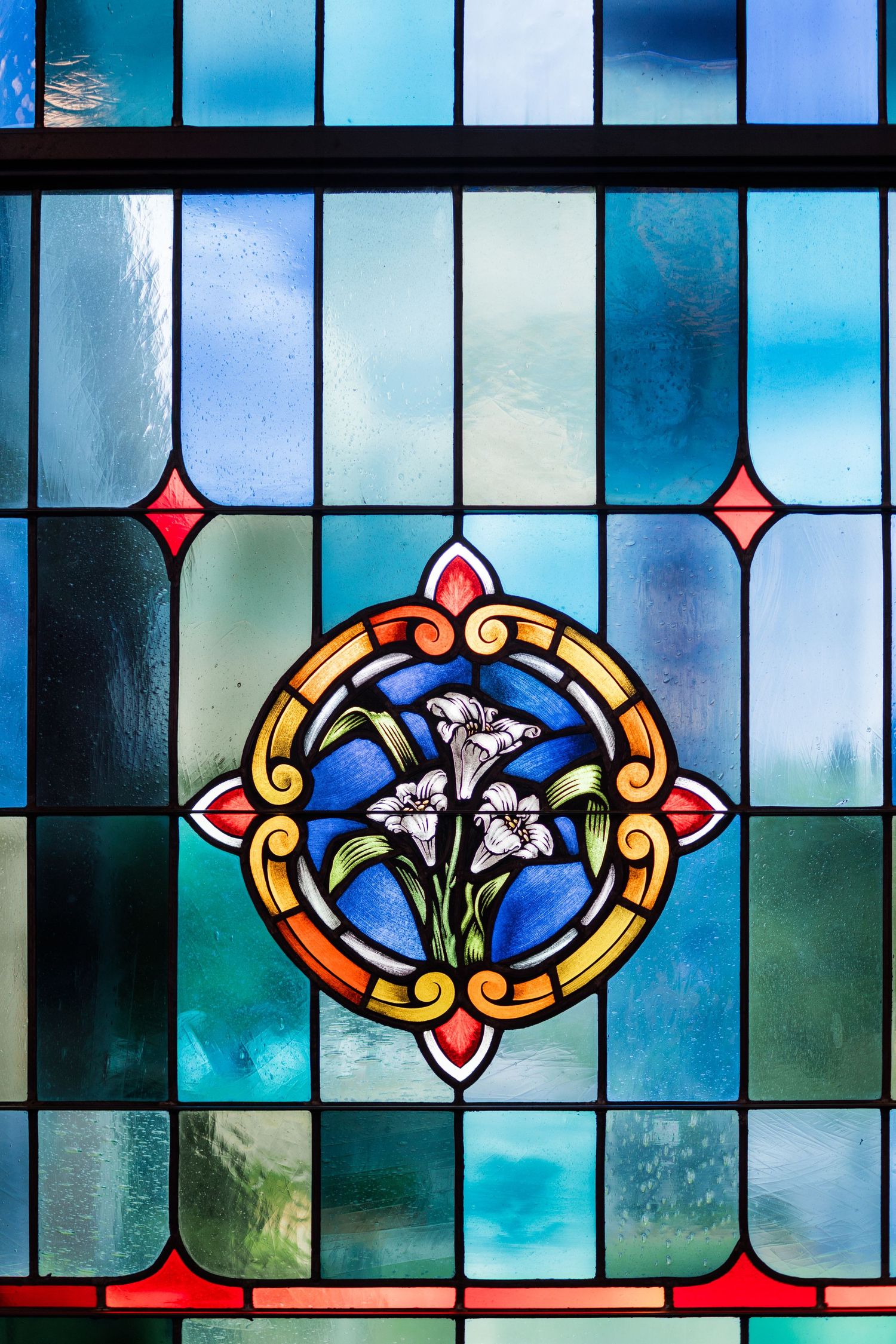 Colorful stained glass church window featuring white lilies in an ornate circular medallion.