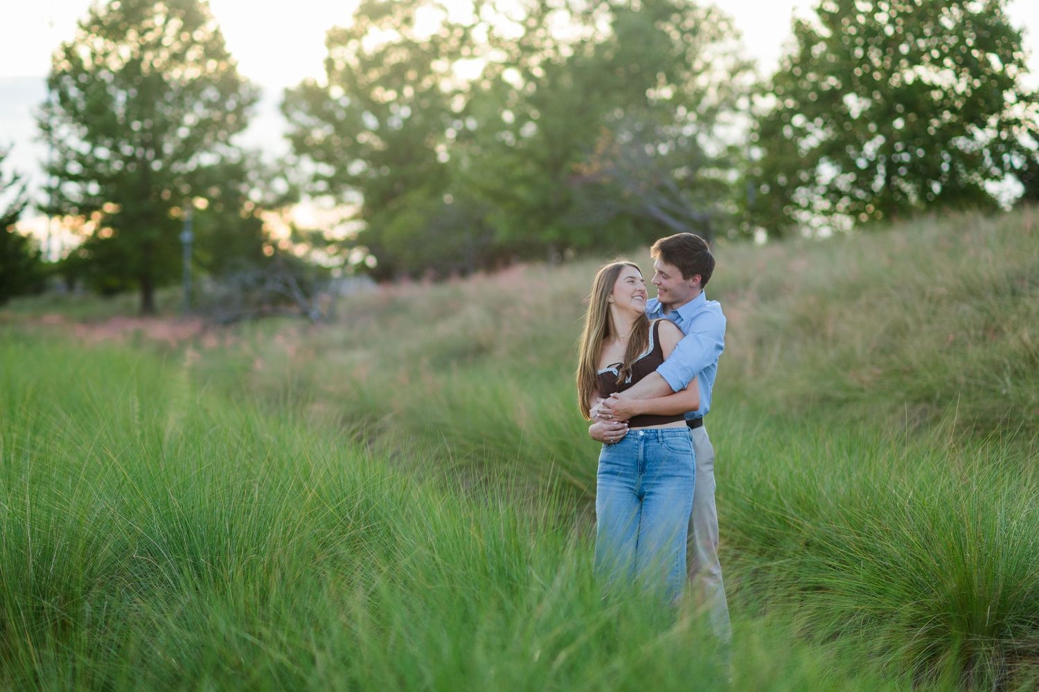 Couple embracing and kissing in a lush green meadow during golden hour sunset outdoors.