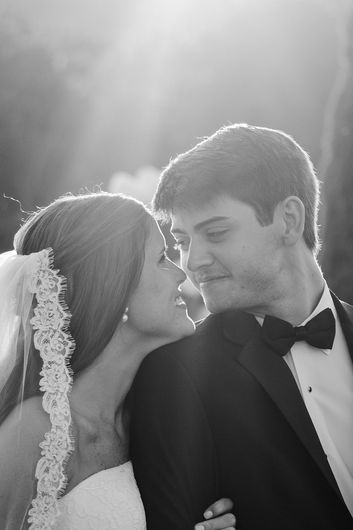 Black and white wedding photo of bride and groom sharing a romantic moment, backlit by soft glowing light.